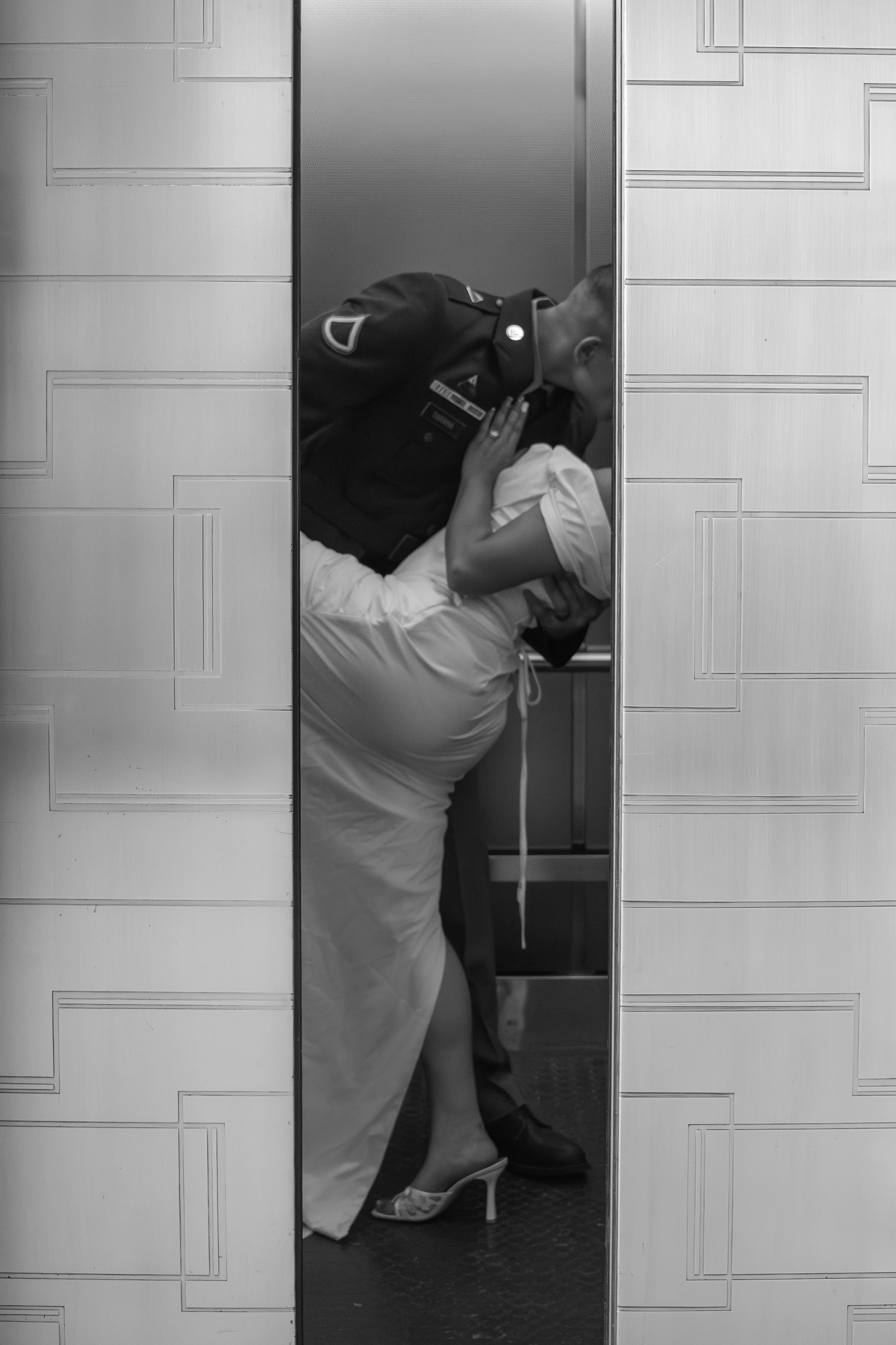 A person in a uniform leaning into an elevator with another person. The scene is in black and white.