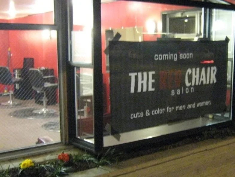 Sign advertising a new salon called 'The Red Chair Salon' with services including cuts and color for men and women, with 'coming soon' written at the top
