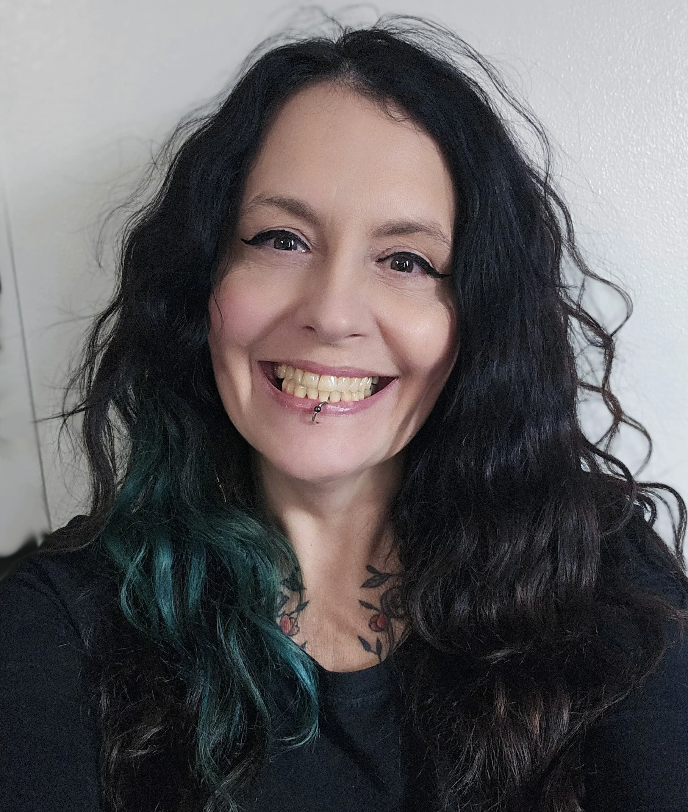 Black-and-white photo of a woman with dark, wavy hair, smiling and showing a side profile with a lip piercing.
