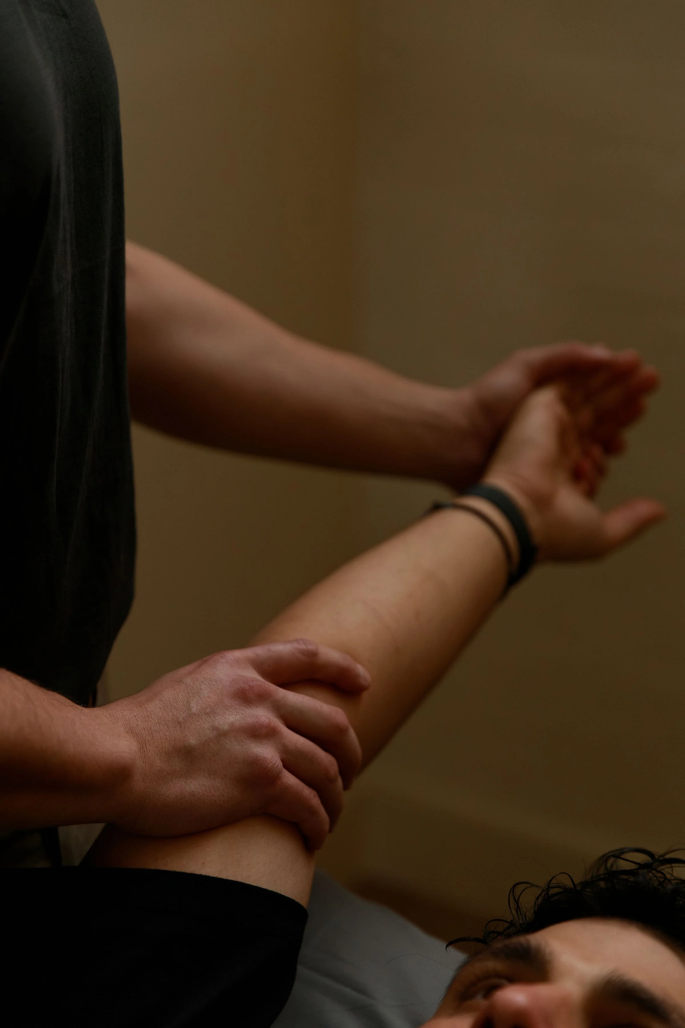 Close-up of multiple people holding hands and arms intertwined, with some individuals wearing bracelets, against a plain background.
