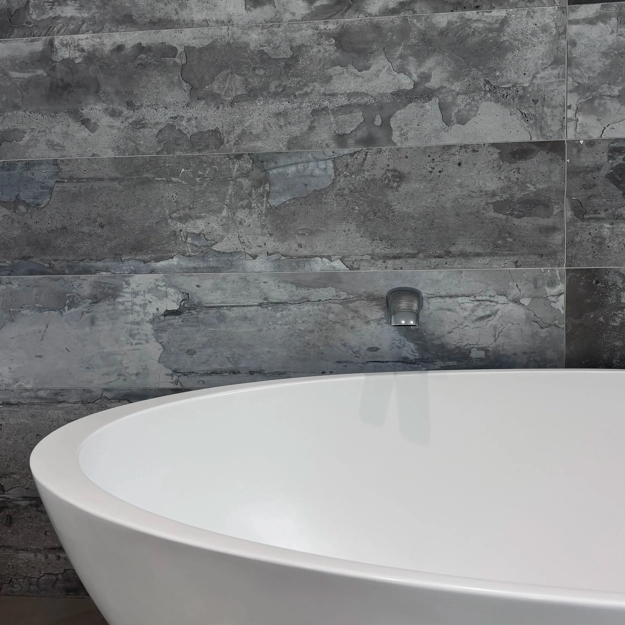 A white bathtub in the foreground with a dark gray, cracked and textured concrete wall in the background.