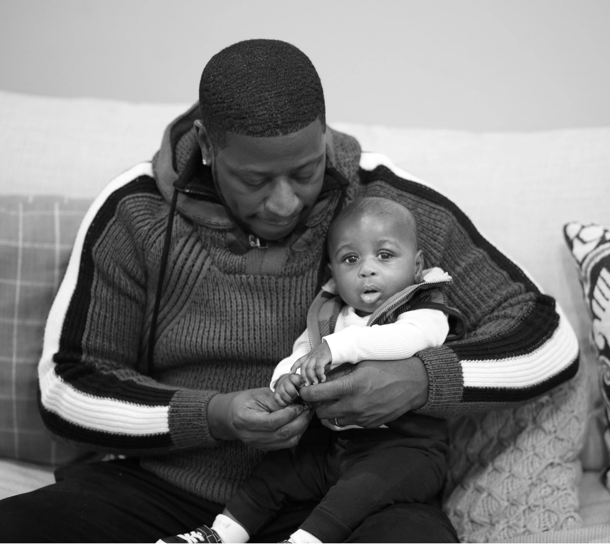 A man holding a young child on his lap, sitting on a couch in an indoor setting.