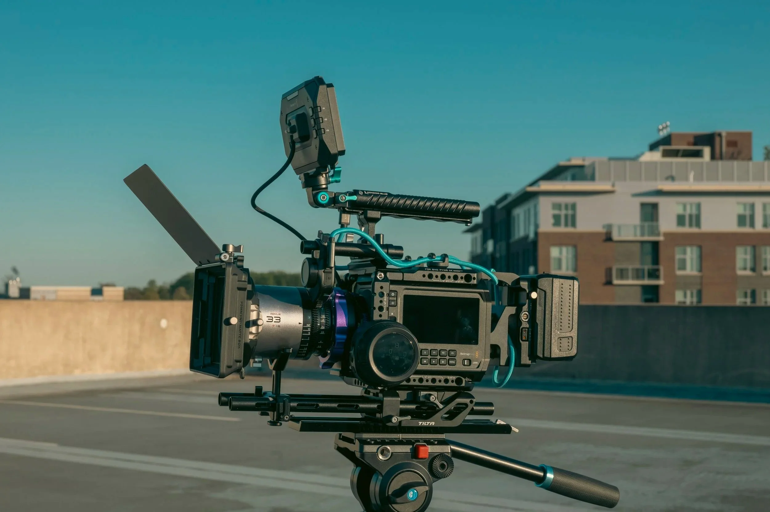 A professional cinema camera setup on a tripod outdoors on a rooftop with buildings in the background.