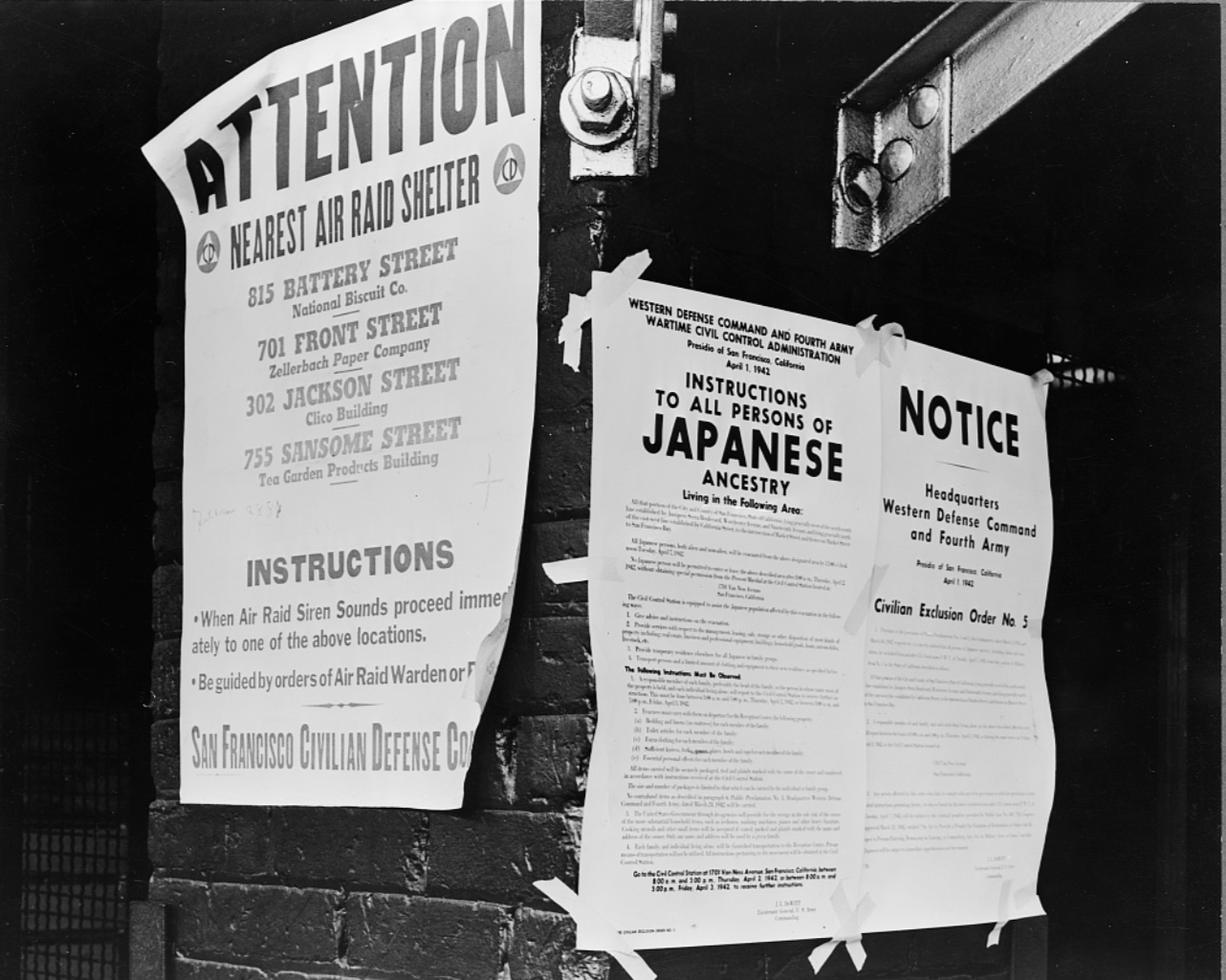 Historical black and white photo of three notices posted on a brick wall, including an air raid shelter notice, a Japanese ancestry notice, and a civil exclusion order notice from World War II era.