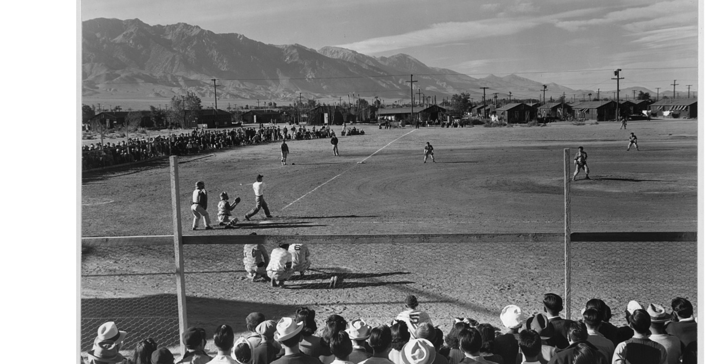 Black and white photograph of a vintage baseball game with players on the field, fans in the stands, and a mountain range in the background.