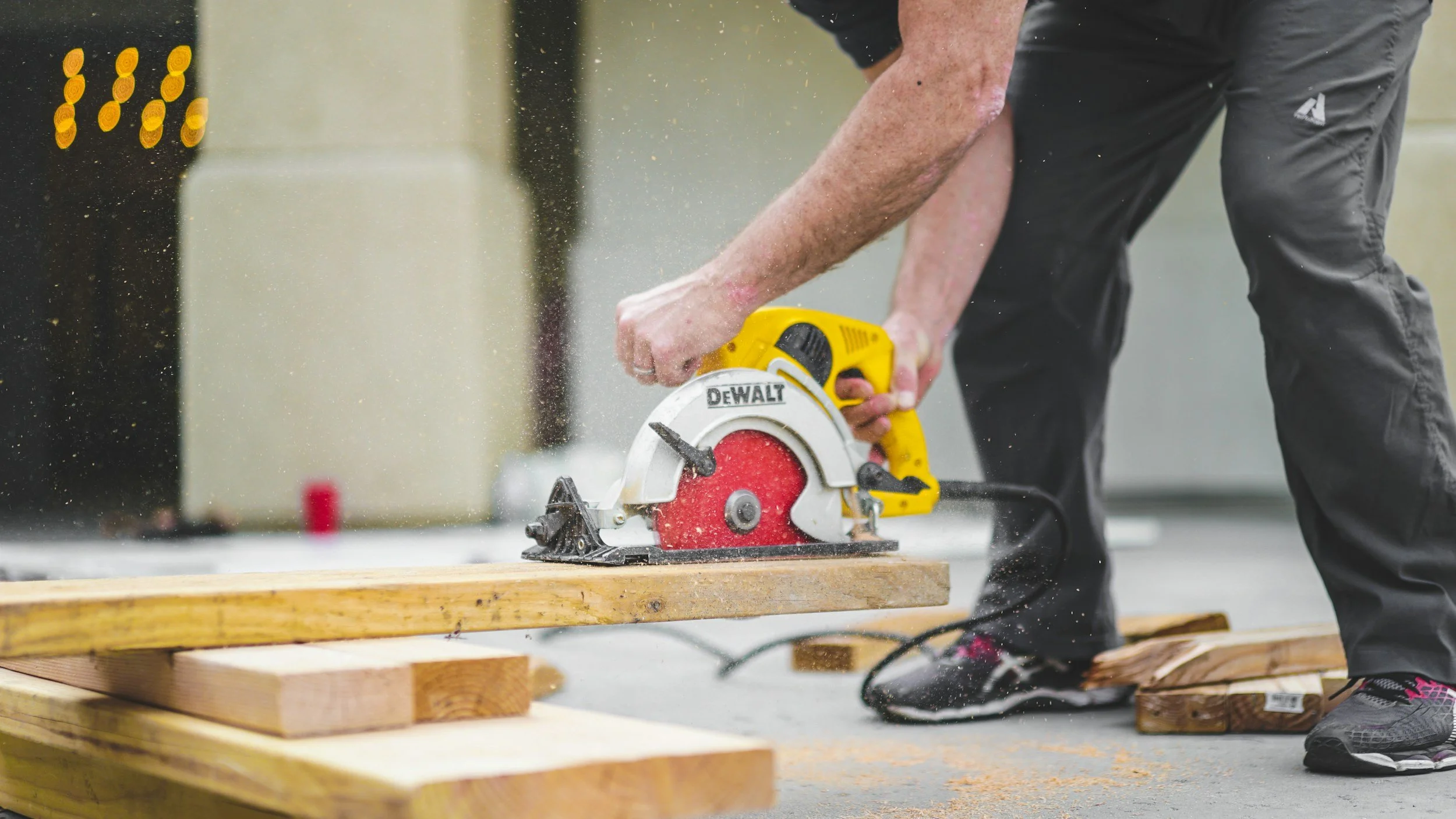 Person using a yellow DeWalt circular saw to cut a wooden board on a workbench with wood pieces around.