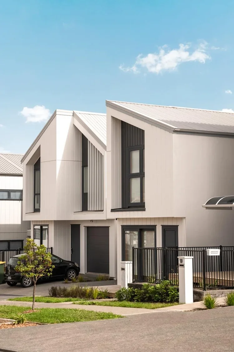 Close-up exterior view of modern new-build residential townhouses featuring off-white vertical cladding, distinctive pitched metal roofs, and contrasting dark window frames.