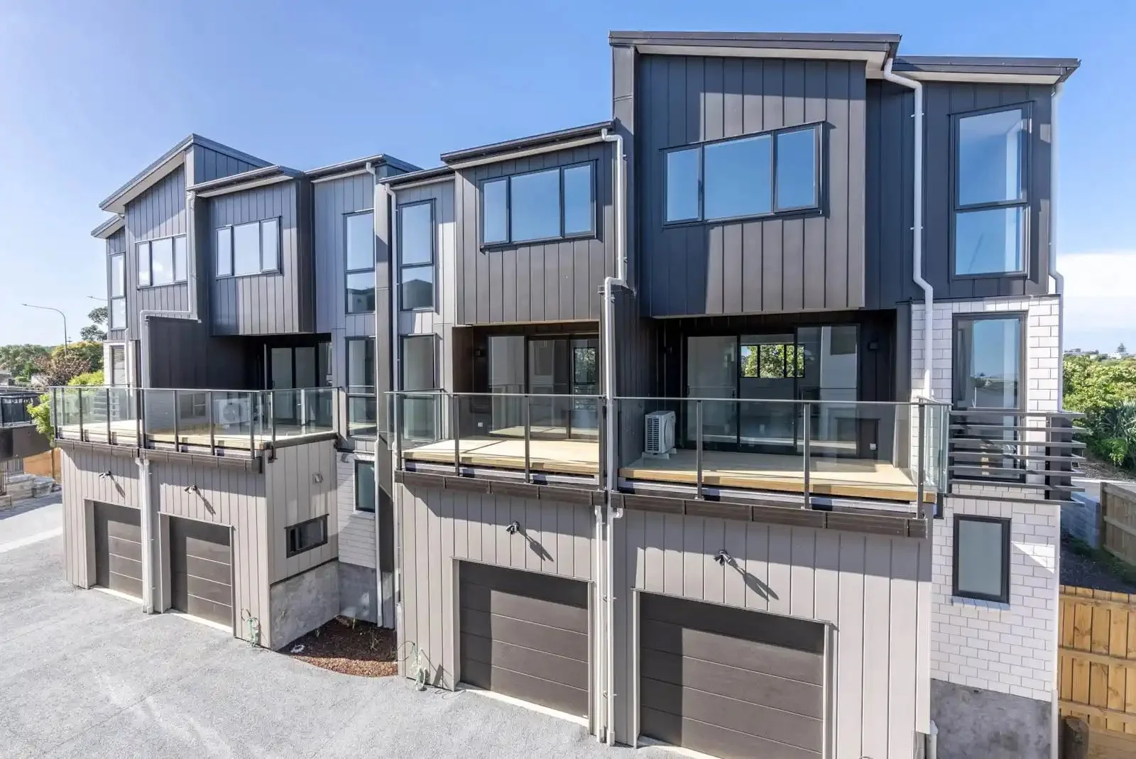 Exterior view of modern three-story new build townhouses with garages and glass balconies, showcasing contemporary grey cladding.