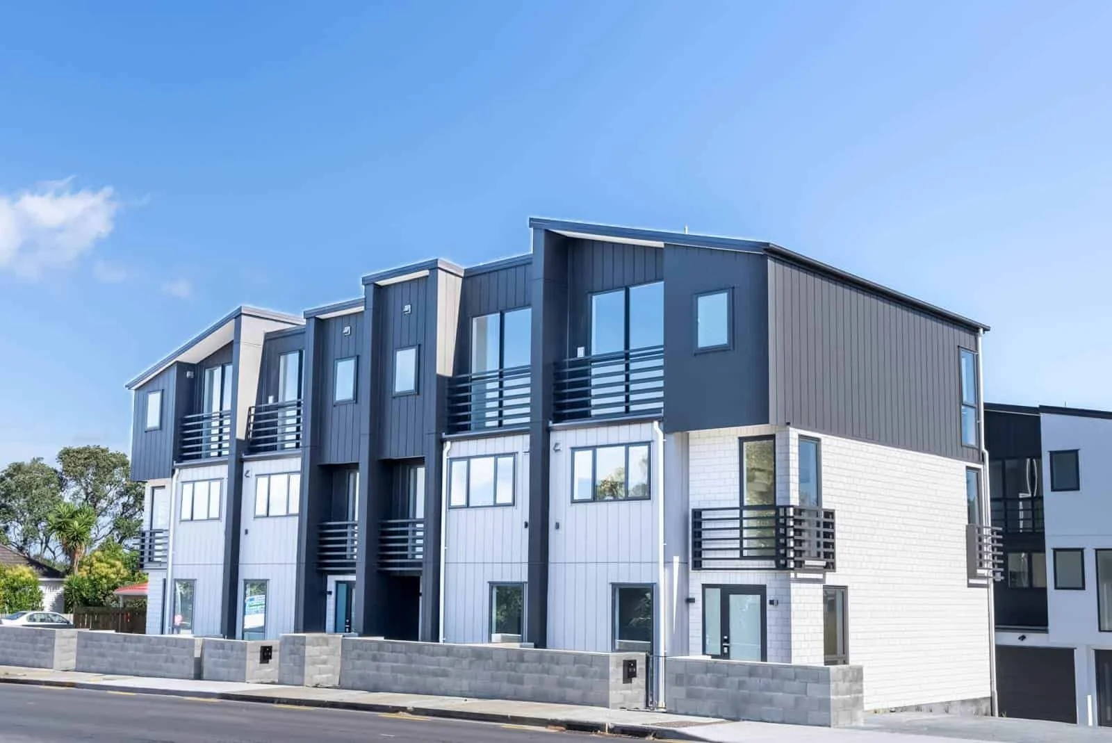 Exterior views of the multi-unit townhouse development, showcasing modern gabled roofs, striking black vertical corrugated metal cladding, and a stepped design on a sloping site.