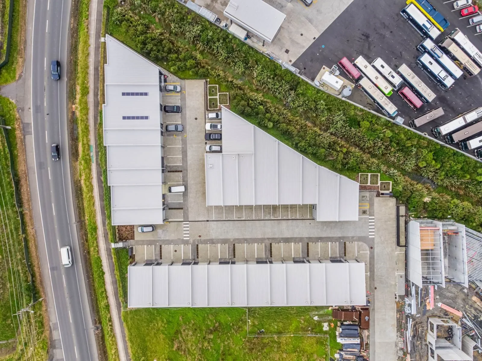 Aerial drone view of a modern commercial warehouse complex featuring multiple industrial units and extensive paved parking facilities. The property is situated adjacent to a main road, highlighting accessible transport links for businesses.