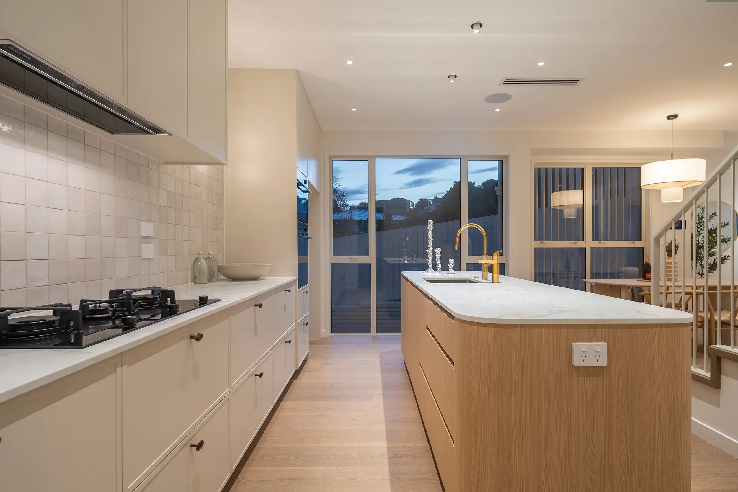 A modern open-concept living area featuring curved white sofas, light wood flooring, a geometric rug, and a sleek black kitchen.