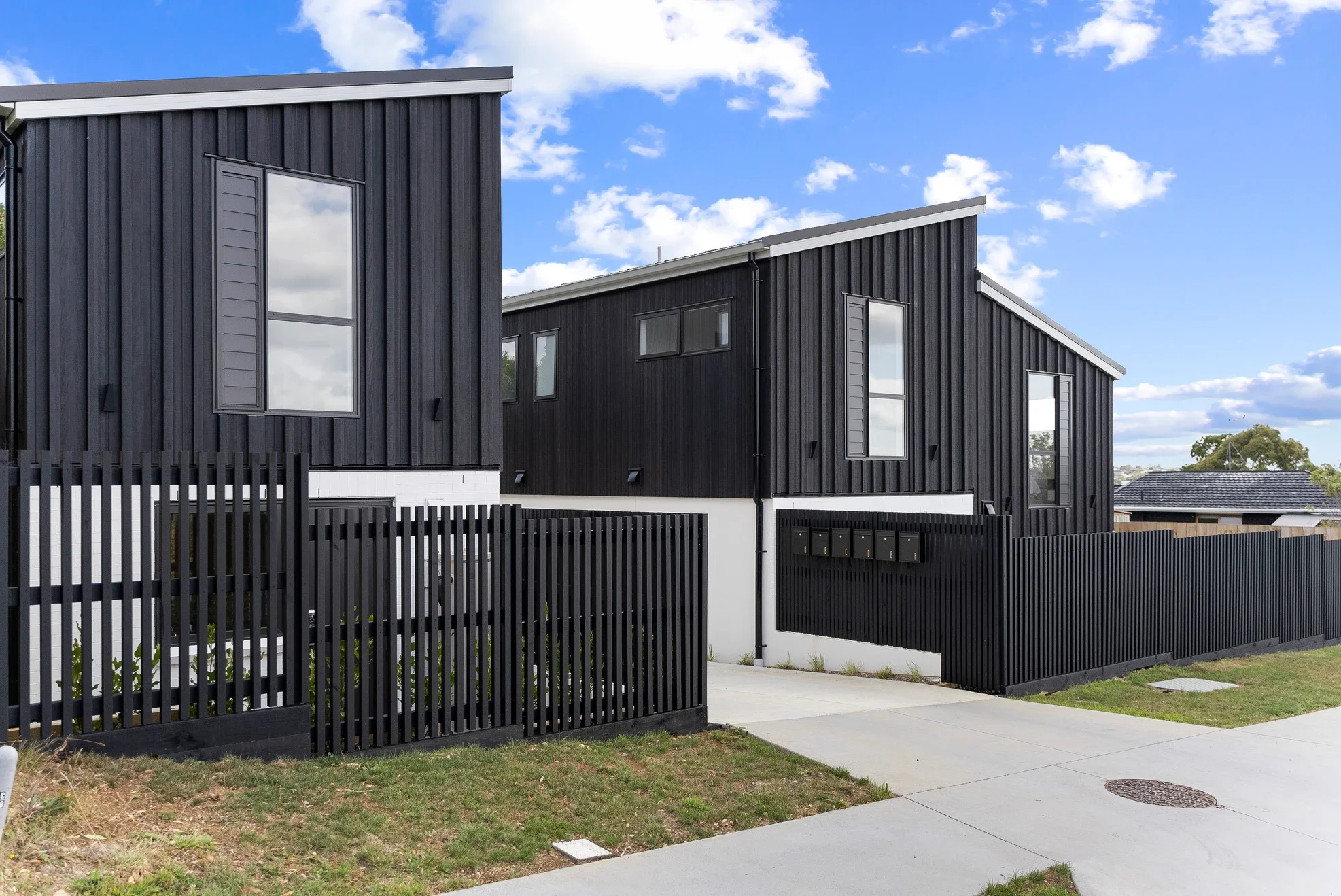 Exterior view of modern multi-story townhouses in Auckland, with integrated ground-floor garages and glass-panelled balconies. 