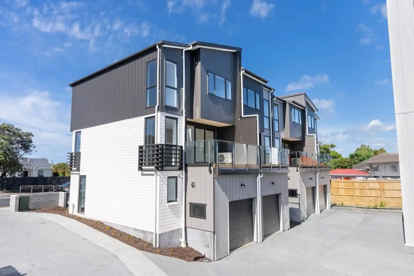 Side exterior of a modern residential townhouse development featuring white brick, grey siding, and a paved driveway.
