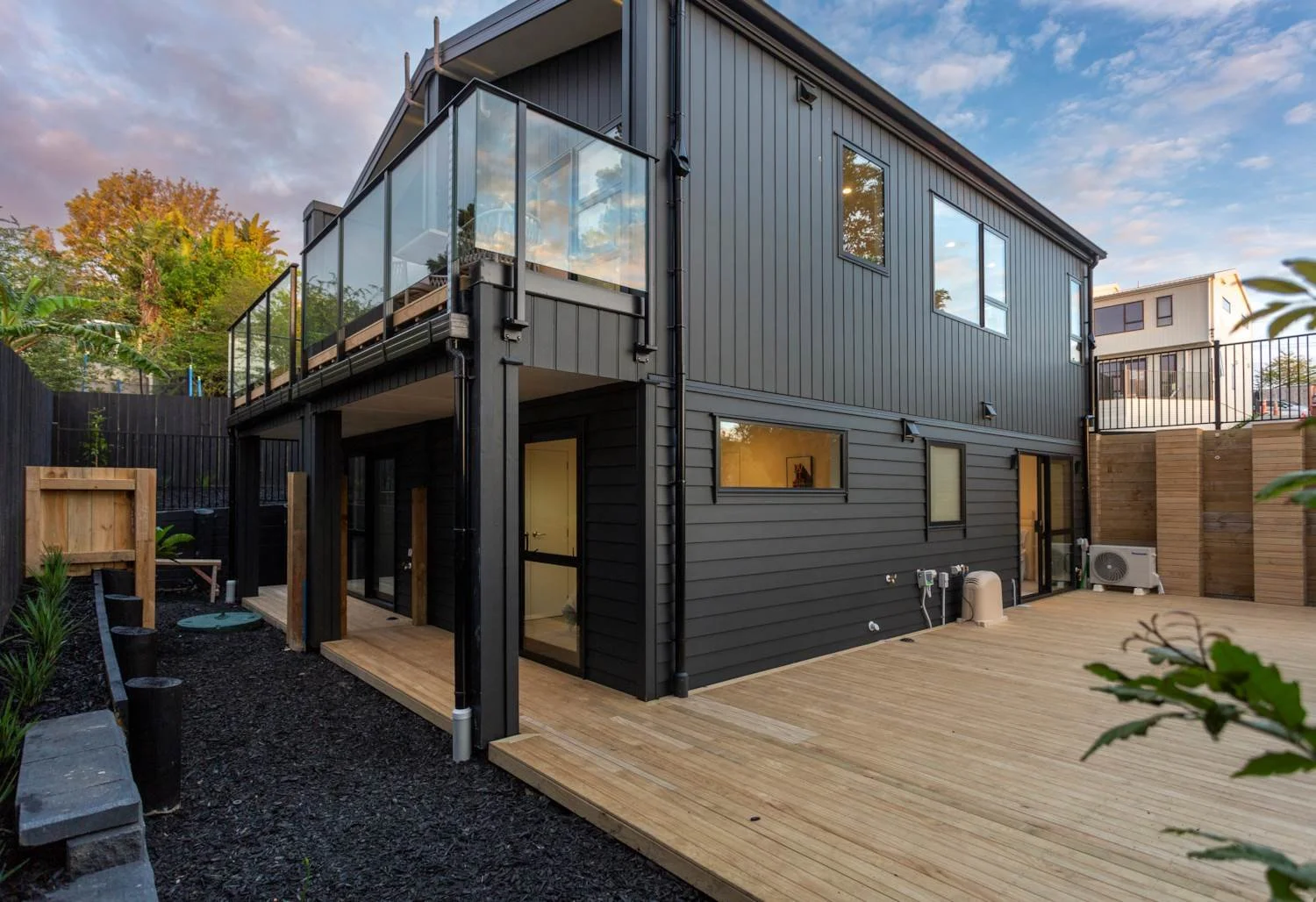 A modern, dark-clad hillside residential project in Glenfield, Auckland, glowing at twilight, showcasing Wonderland Construction Group's innovative building capabilities on sloping sections.