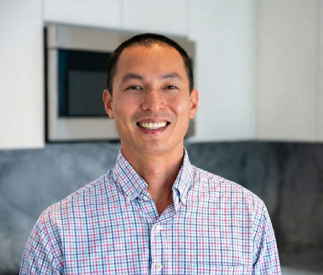 Man smiling in a kitchen, wearing a checked shirt.