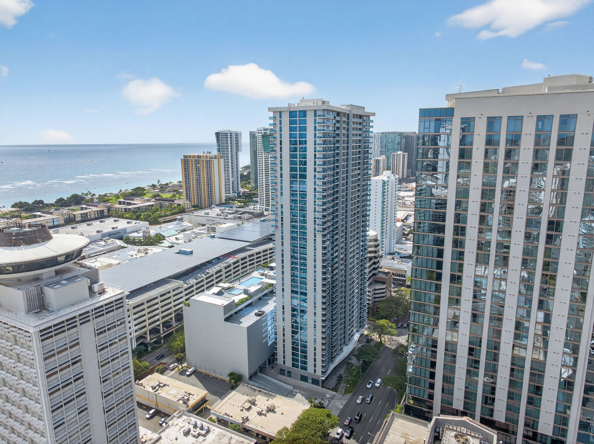 View of a city skyline with tall modern high-rise buildings near the ocean, under a blue sky with a few clouds.