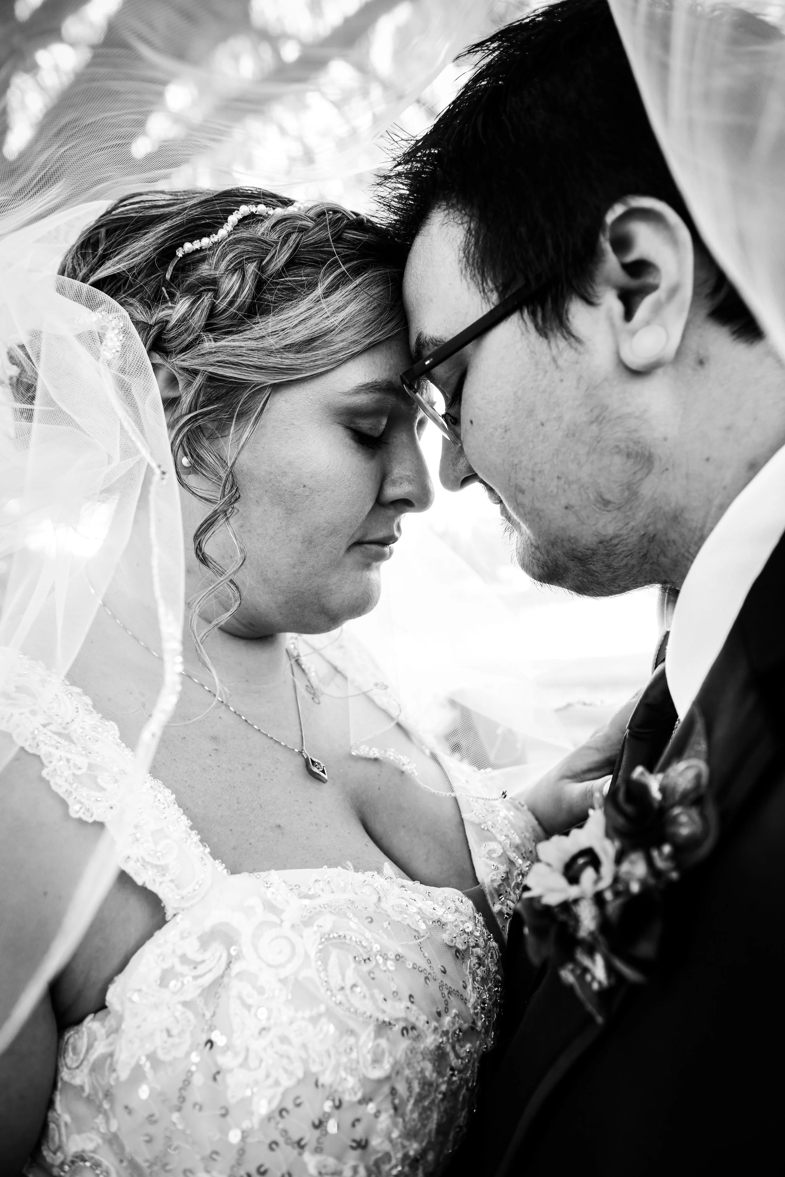 A black-and-white photo of a bride and groom with foreheads touching, eyes closed, sharing an intimate moment during their wedding.