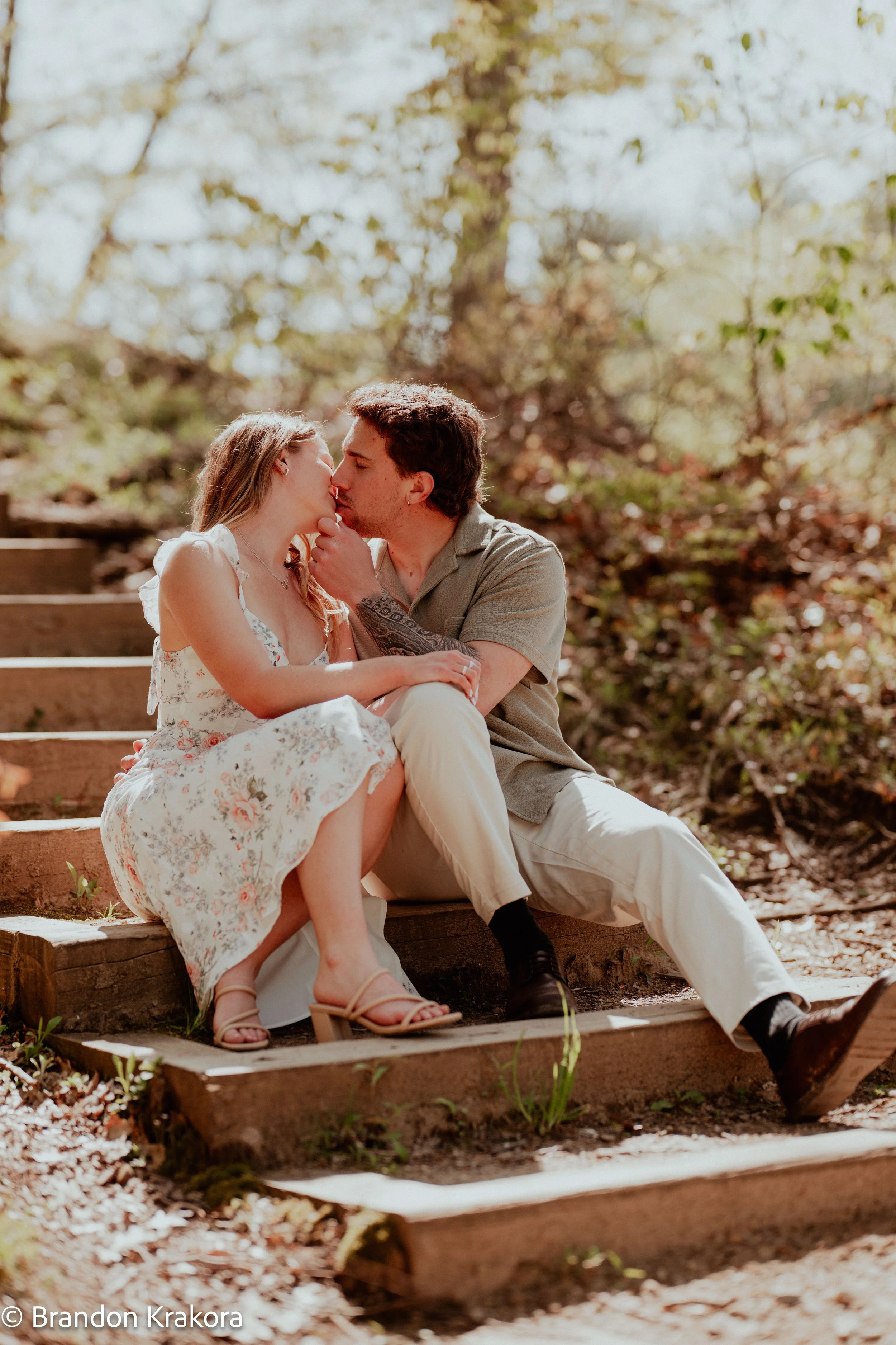 A young couple sharing a kiss while sitting on wooden steps outdoors during daytime.