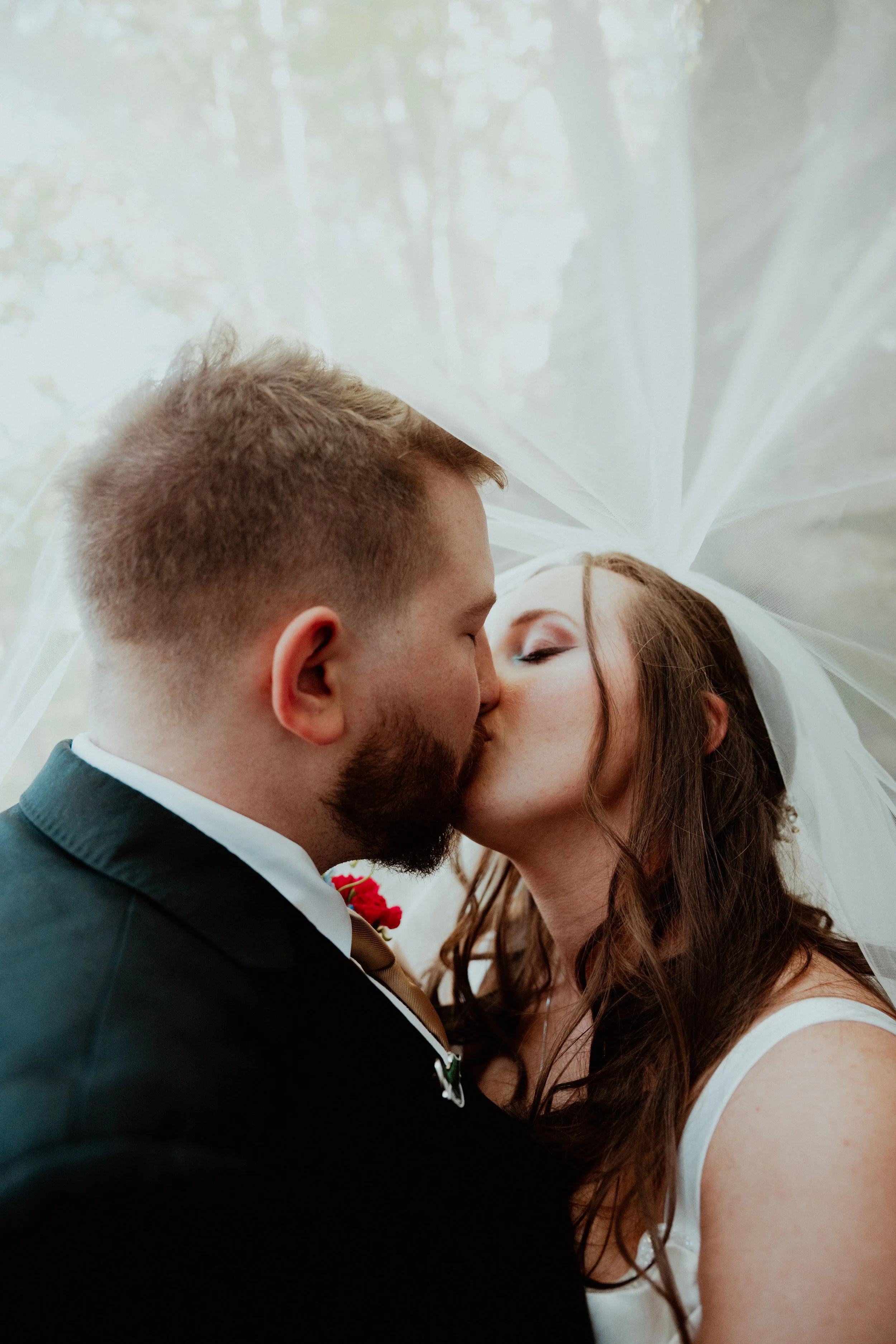 A couple sharing a kiss, likely at their wedding, with the bride wearing a veil and the groom in a tuxedo.