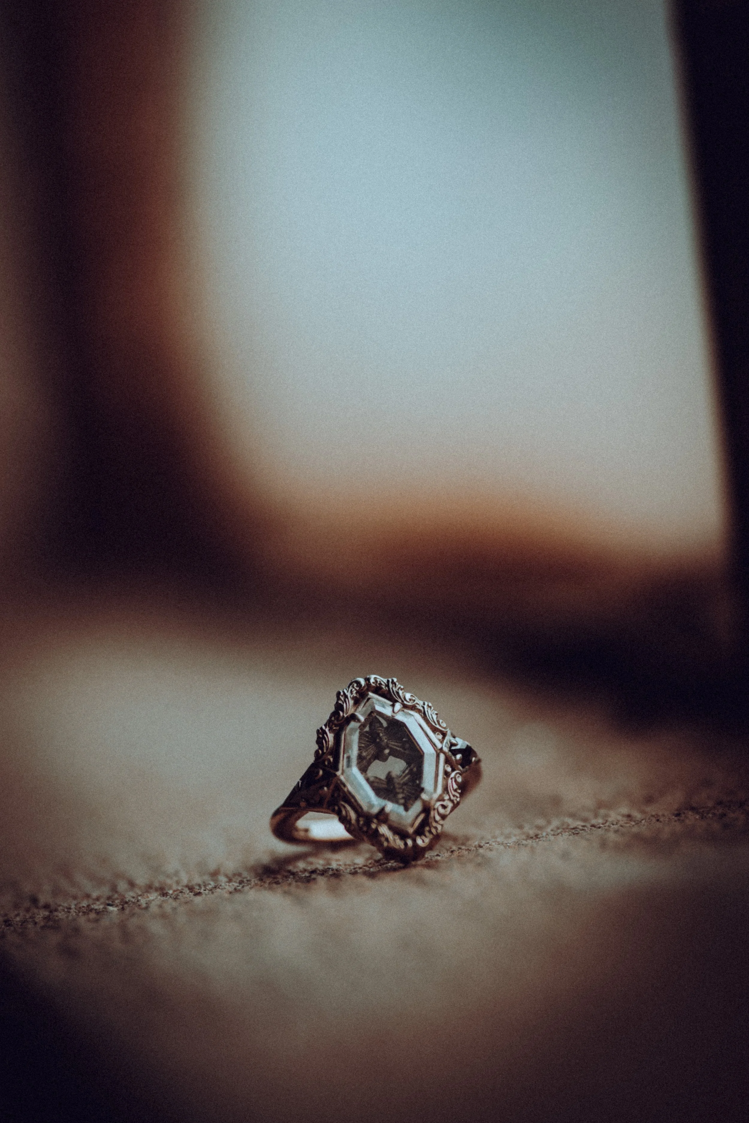 Close-up of an ornate ring with a large gemstone, resting on a textured surface with blurred background.