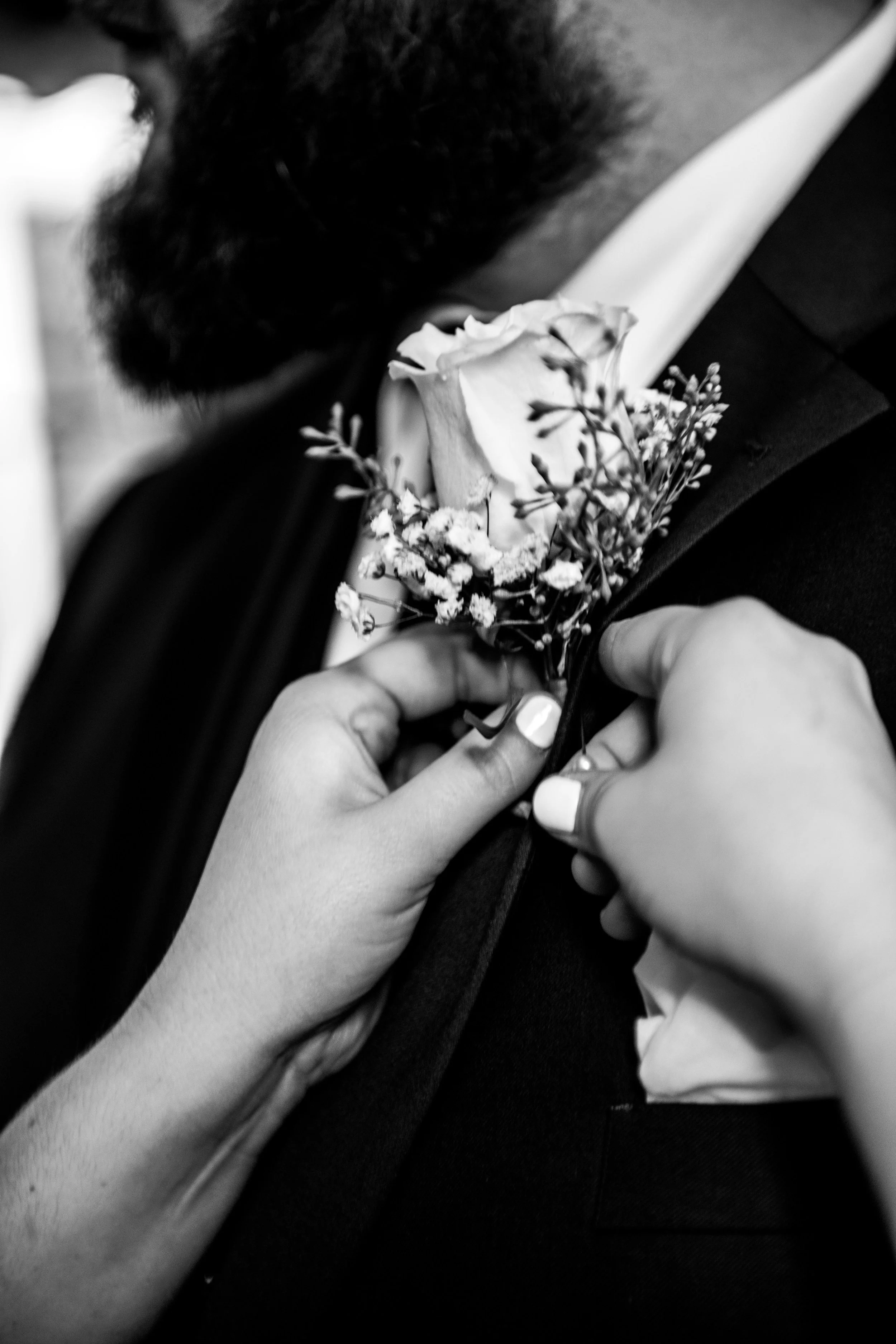 A person in a suit with a boutonniere being pinned on by another person, black and white photo.