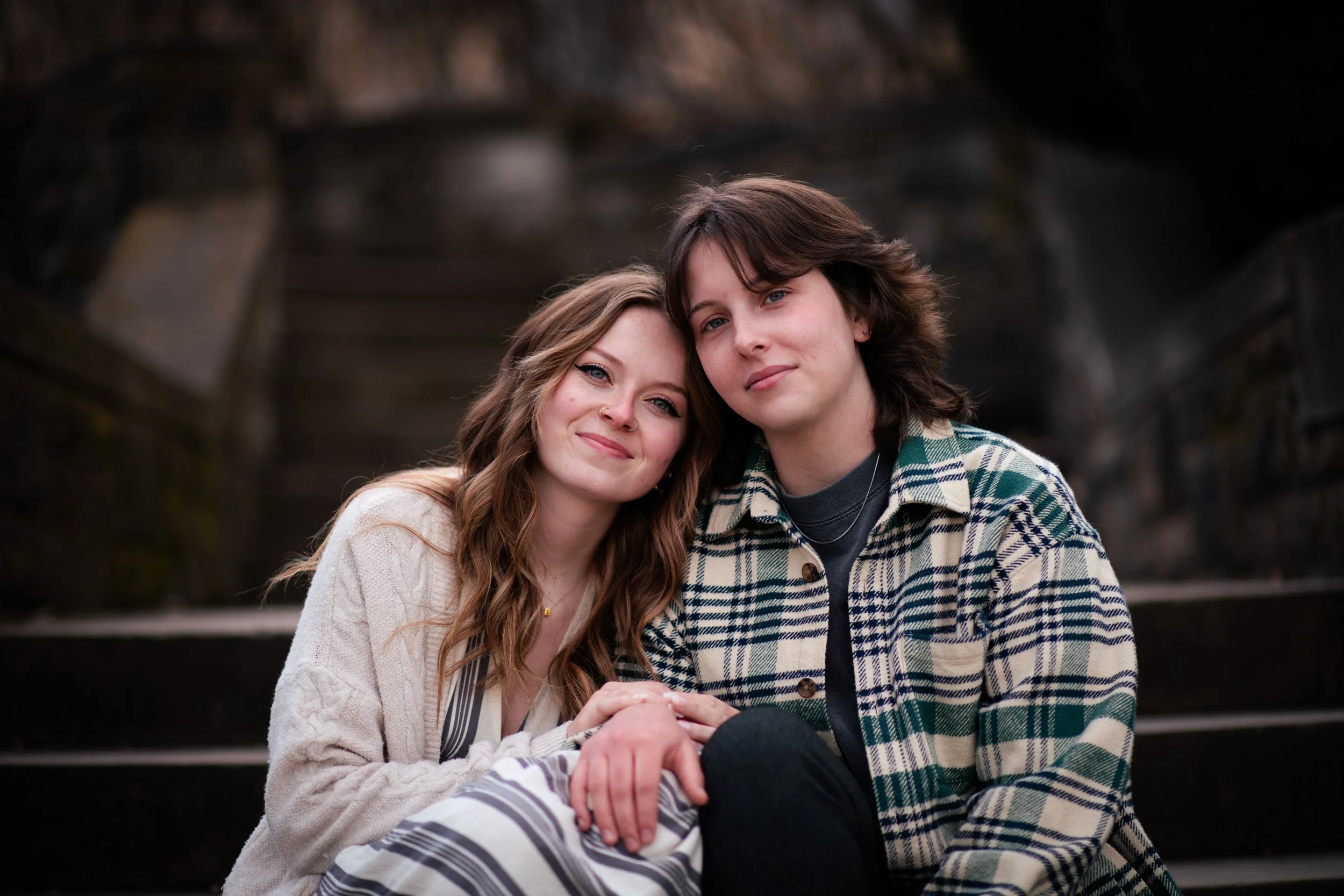 A young couple sitting close together on outdoor stairs, smiling and holding hands.
