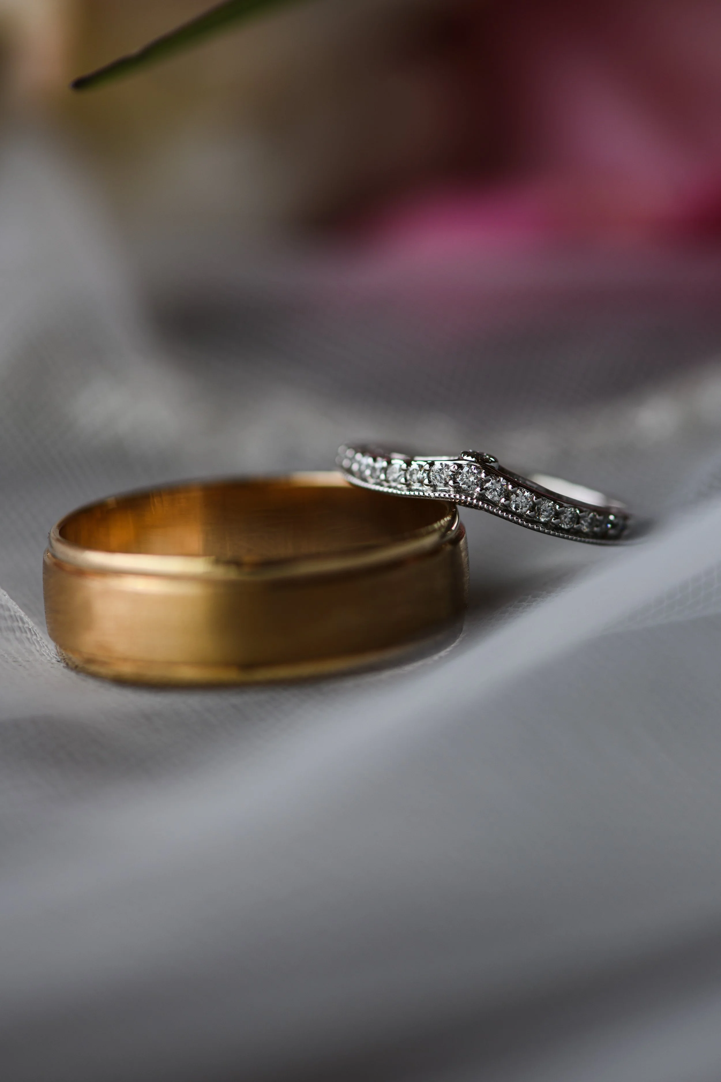 Close-up of two wedding rings: a plain gold band and a diamond-studded silver band on a white fabric surface.