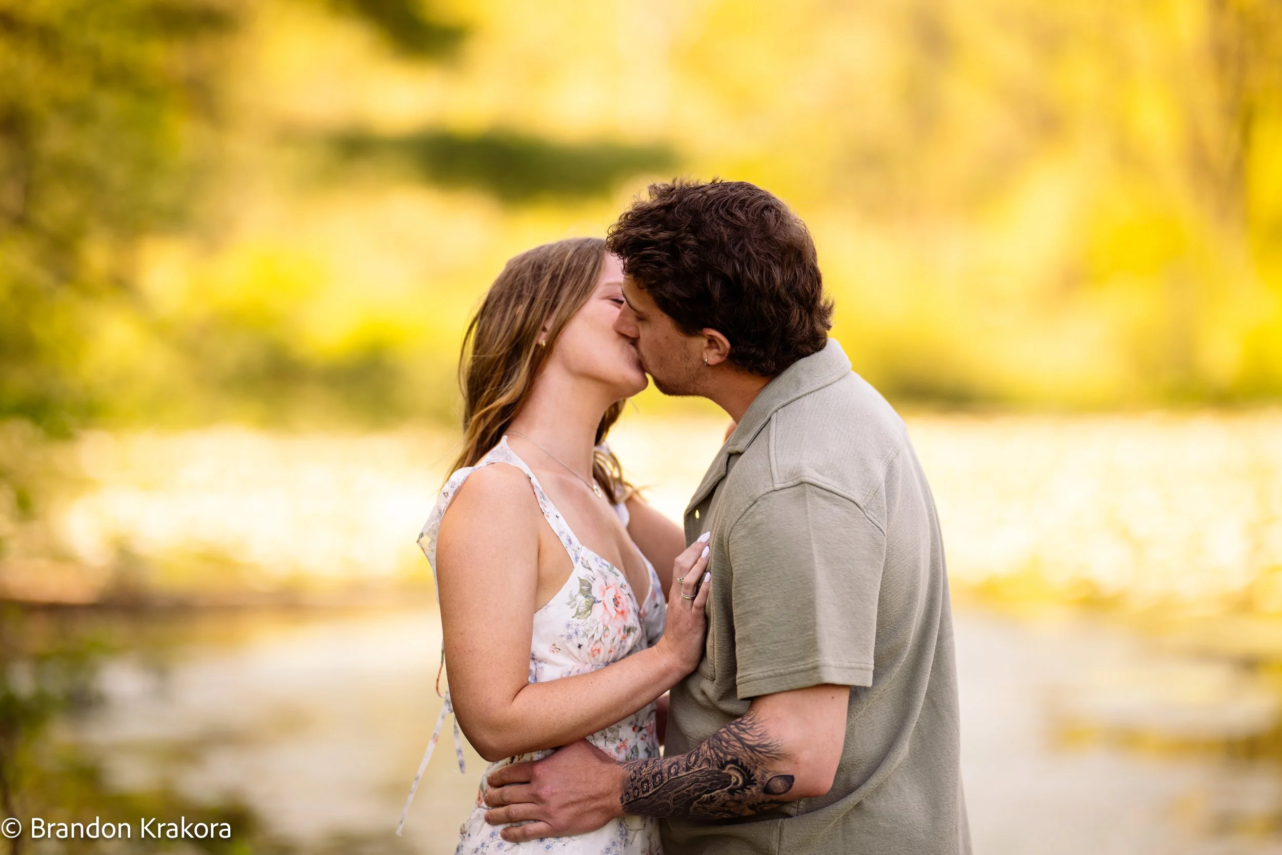 A young couple kissing outdoors in a park with yellow autumn leaves in the background.