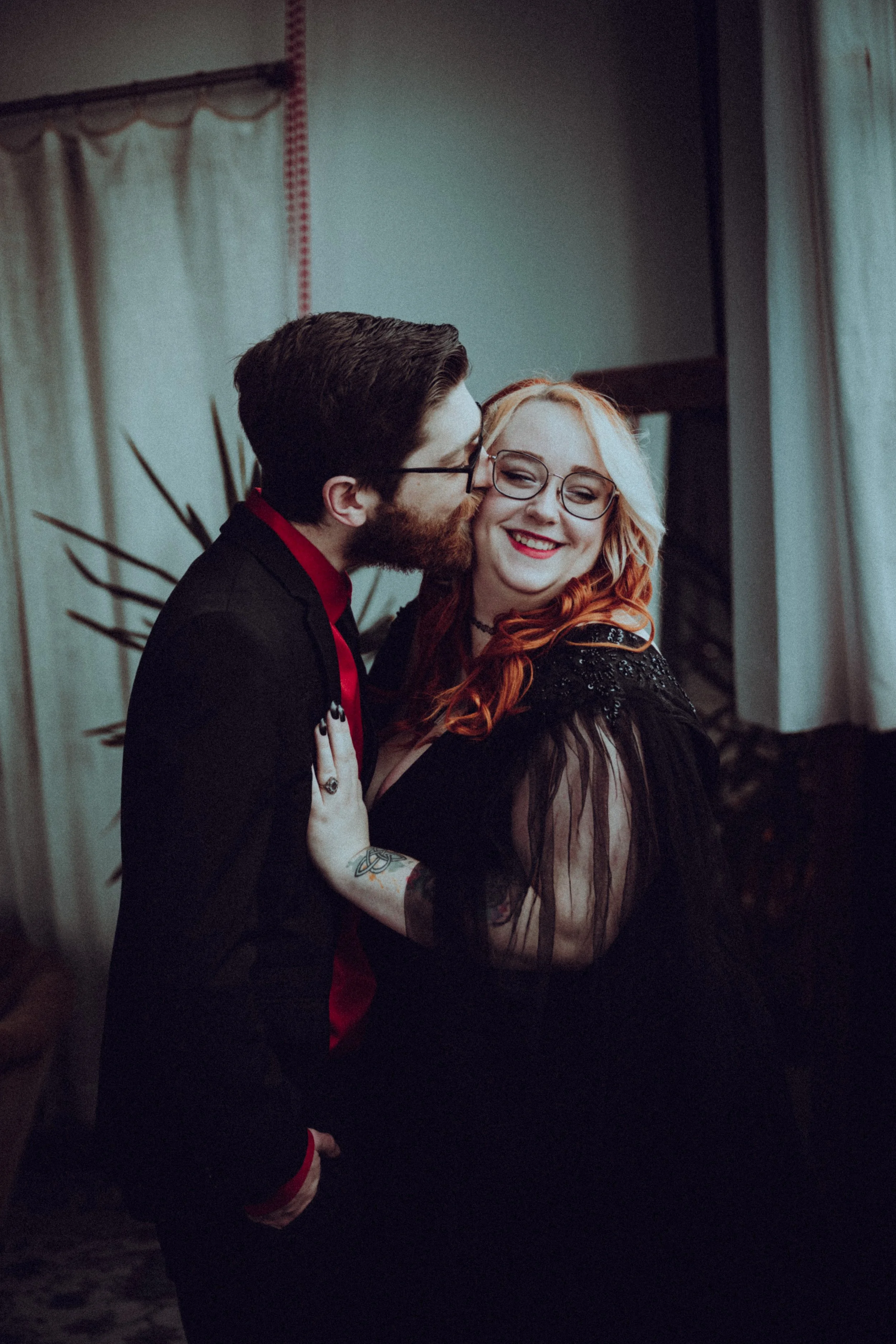 A man and a woman are sharing a kiss and smiling indoors, with the woman showing affection and happiness.