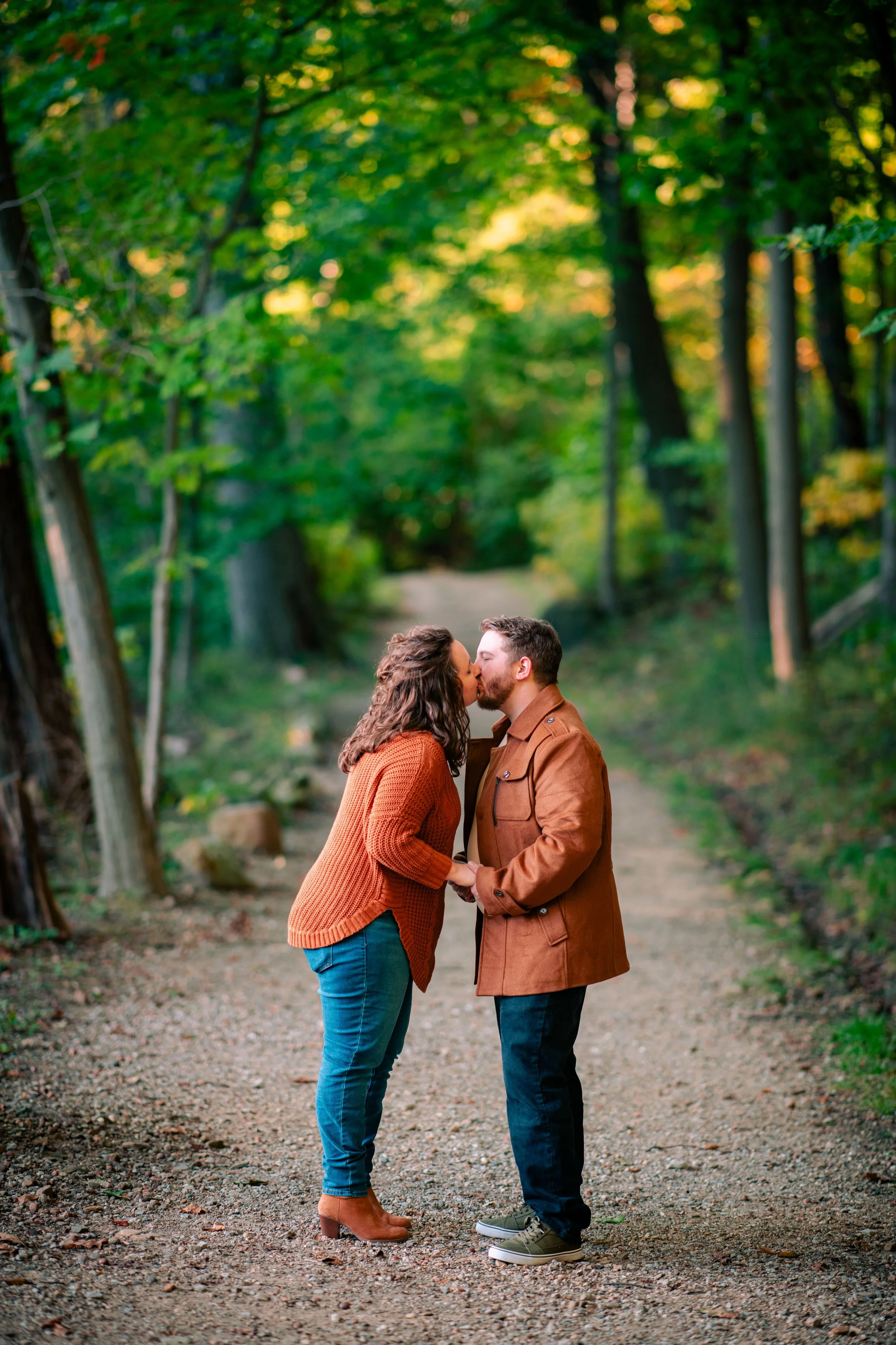 A couple kissing in a forested park during daytime.