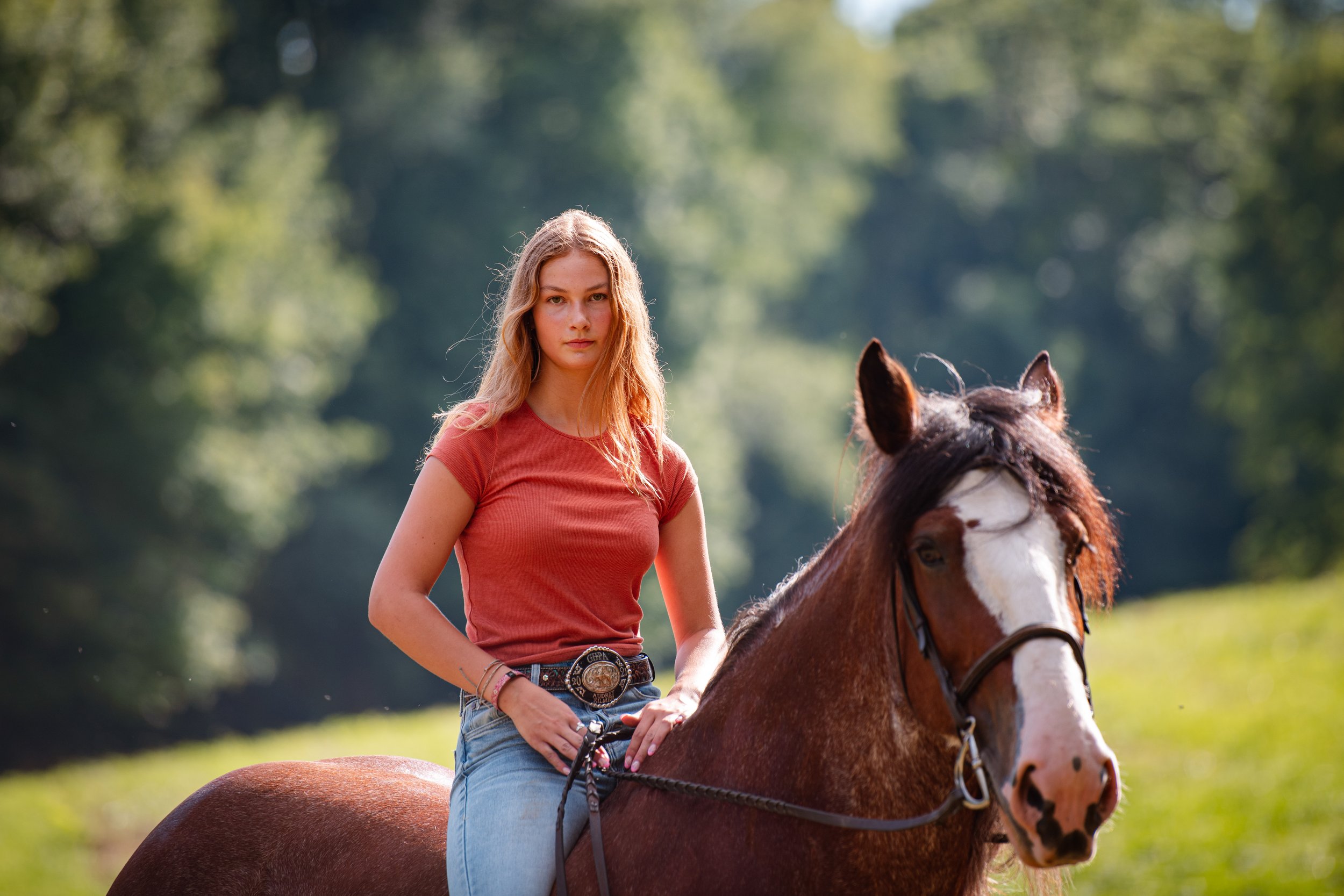 Young woman riding a brown and white horse in a lush green outdoor setting.