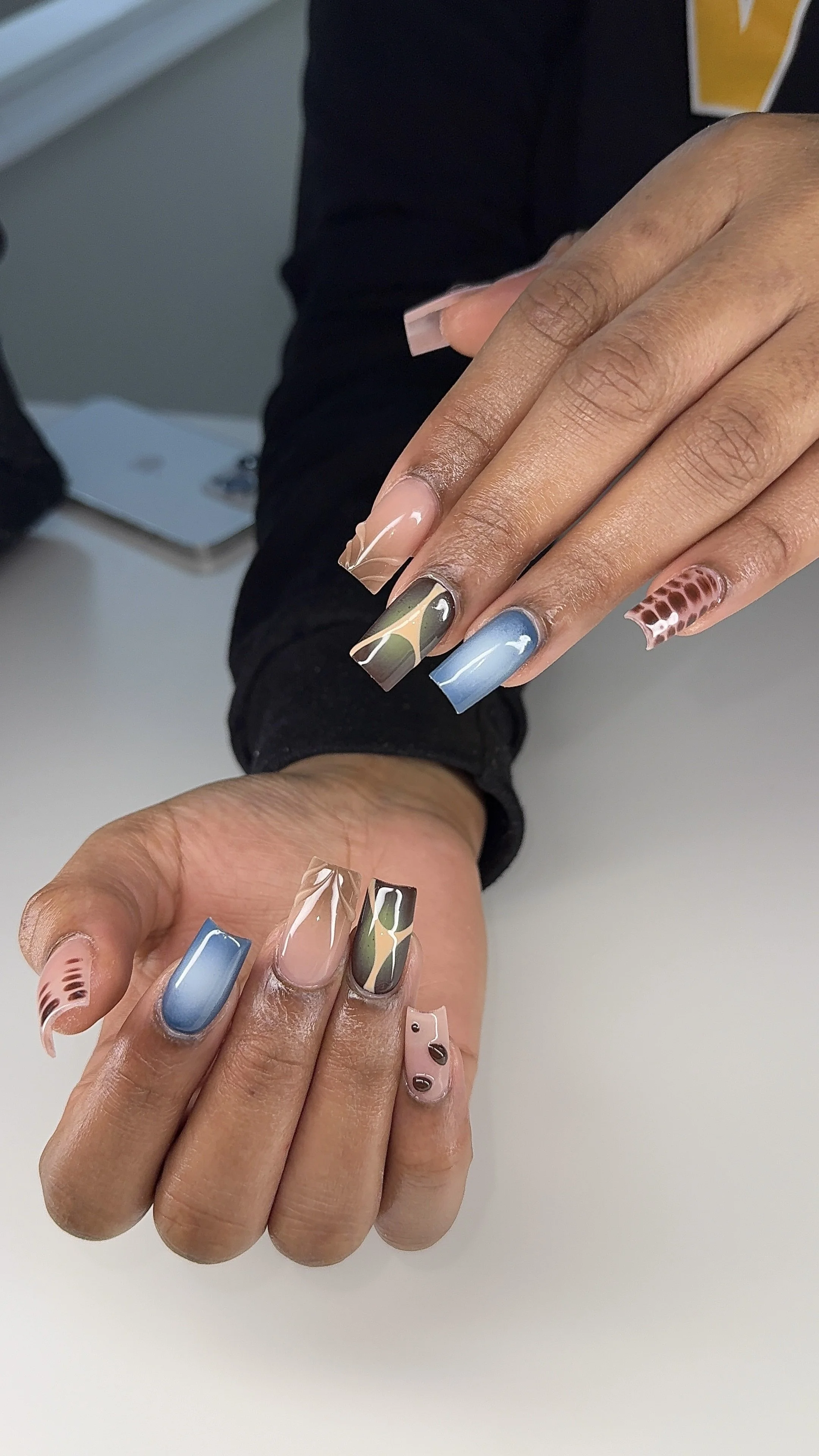 Close-up of manicured nails with various designs and colors, including blue, beige, green, and pink with abstract and animal print patterns.