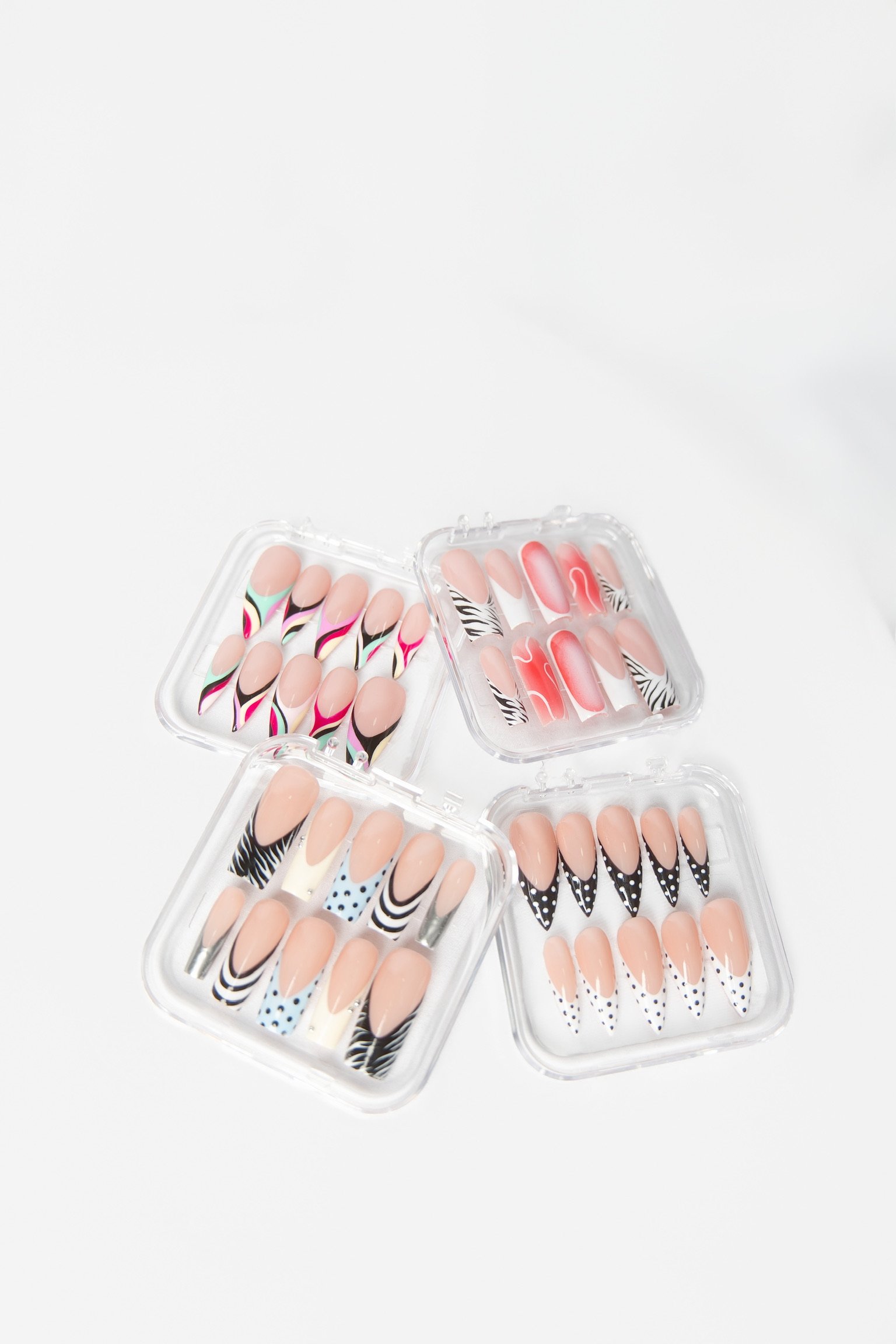 Four clear plastic cases containing colorful, patterned press-on nail sets on a white background.