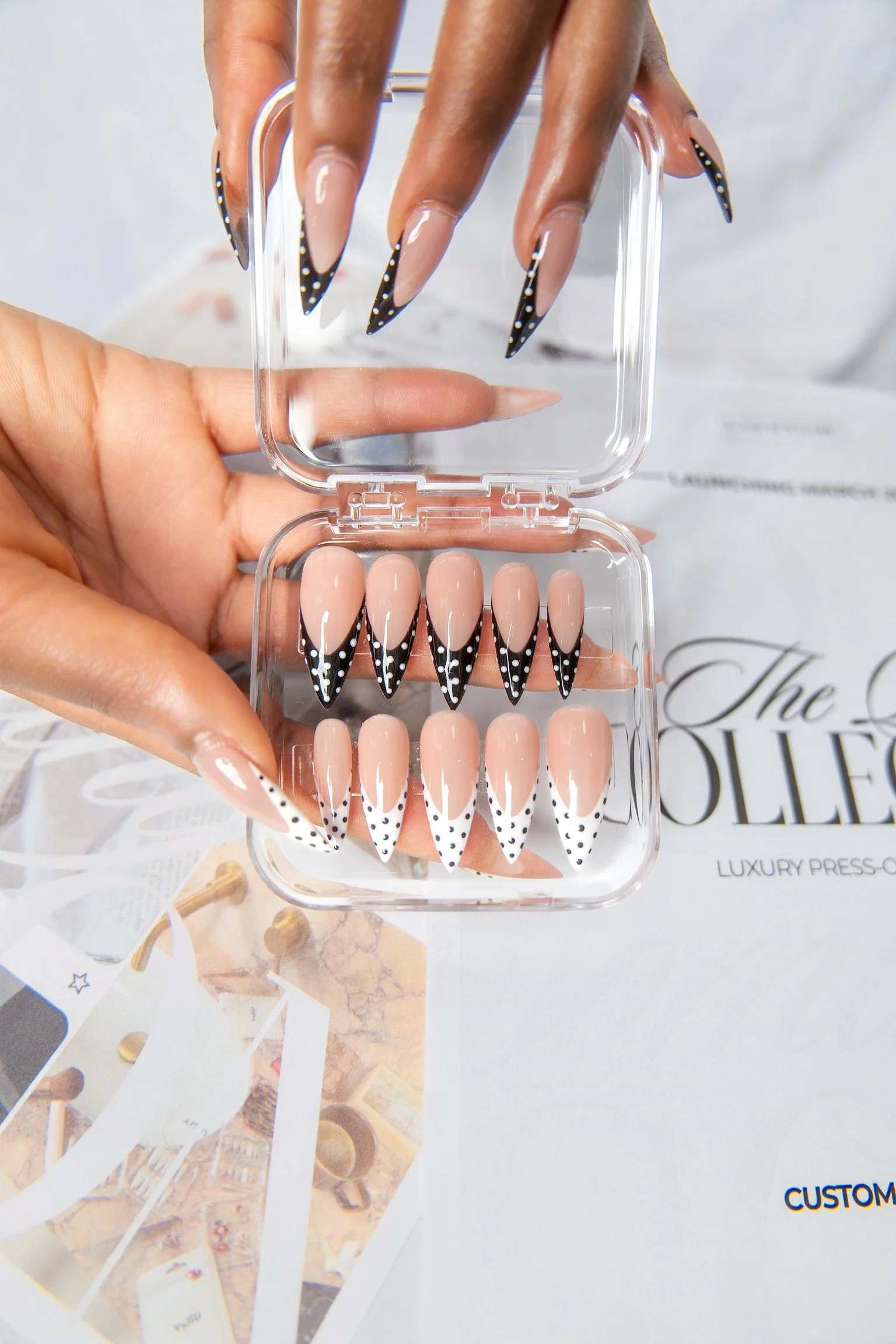 A hand holding a mini case of artificial nails with a black and white polka dot pattern on a beige base.