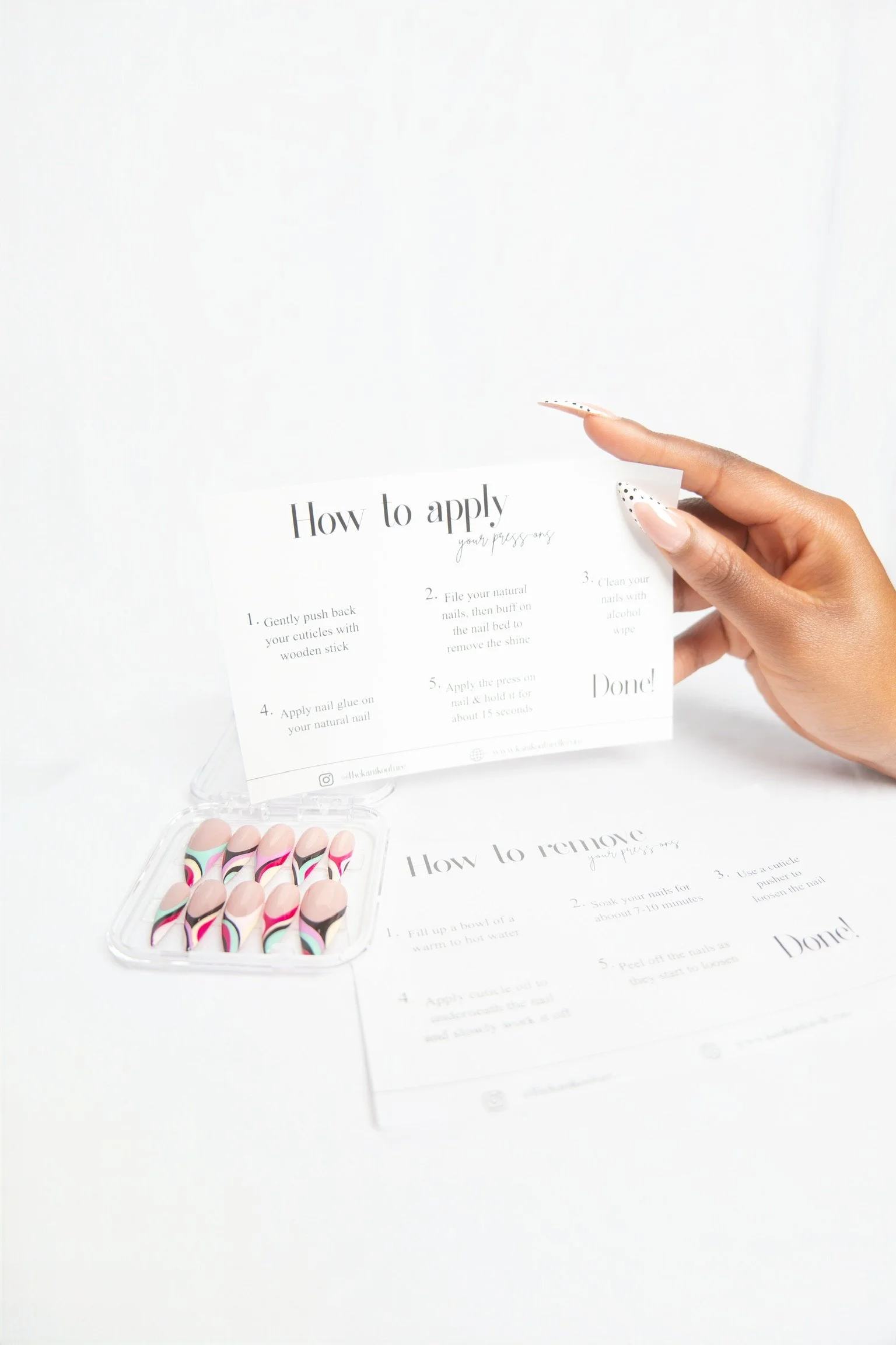 A hand holding a card with nail application instructions next to a small container of colorful artificial nails on a white surface.
