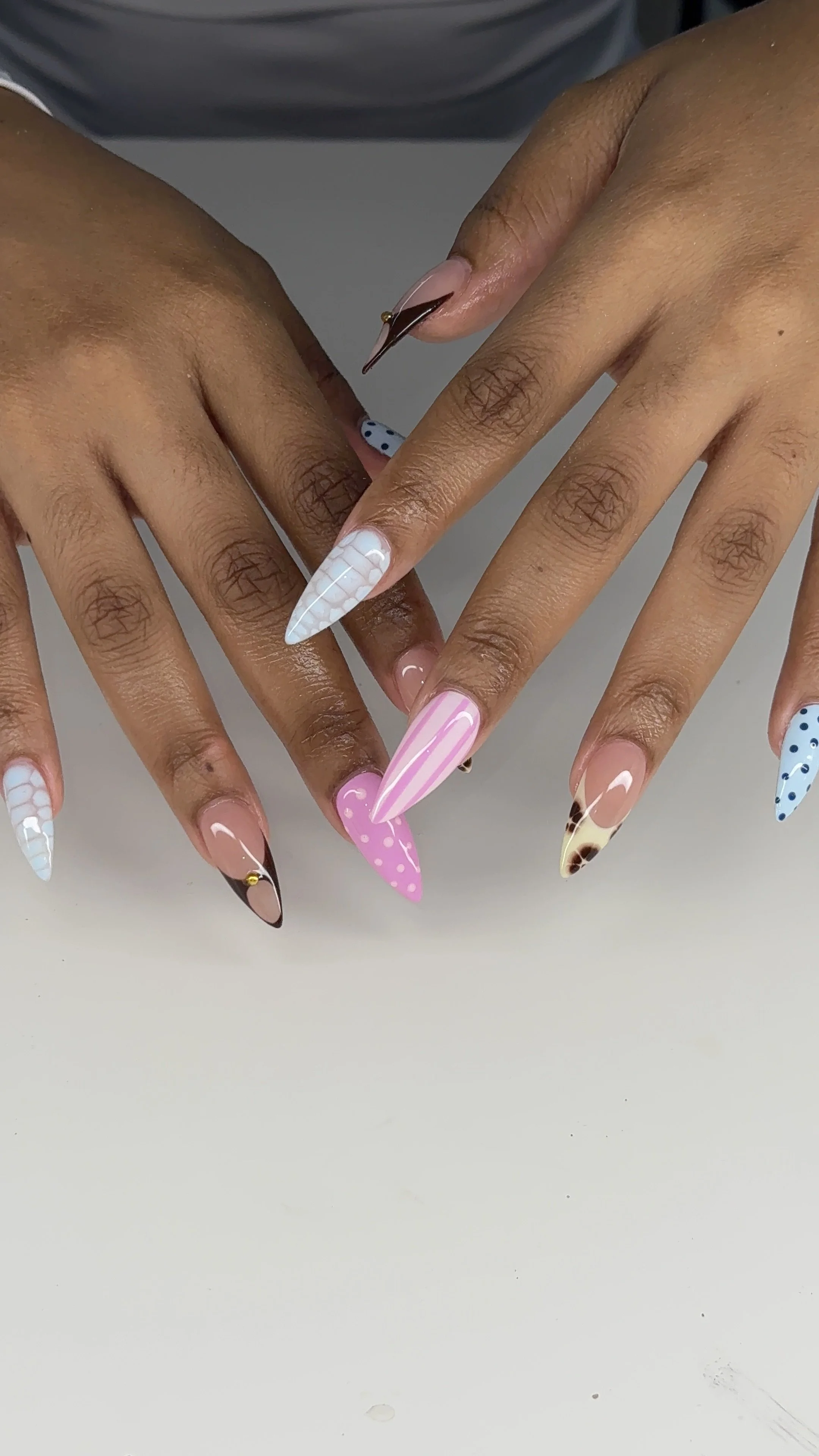 Nail art with various pastel colors, patterns, and designs on long, pointed nails.