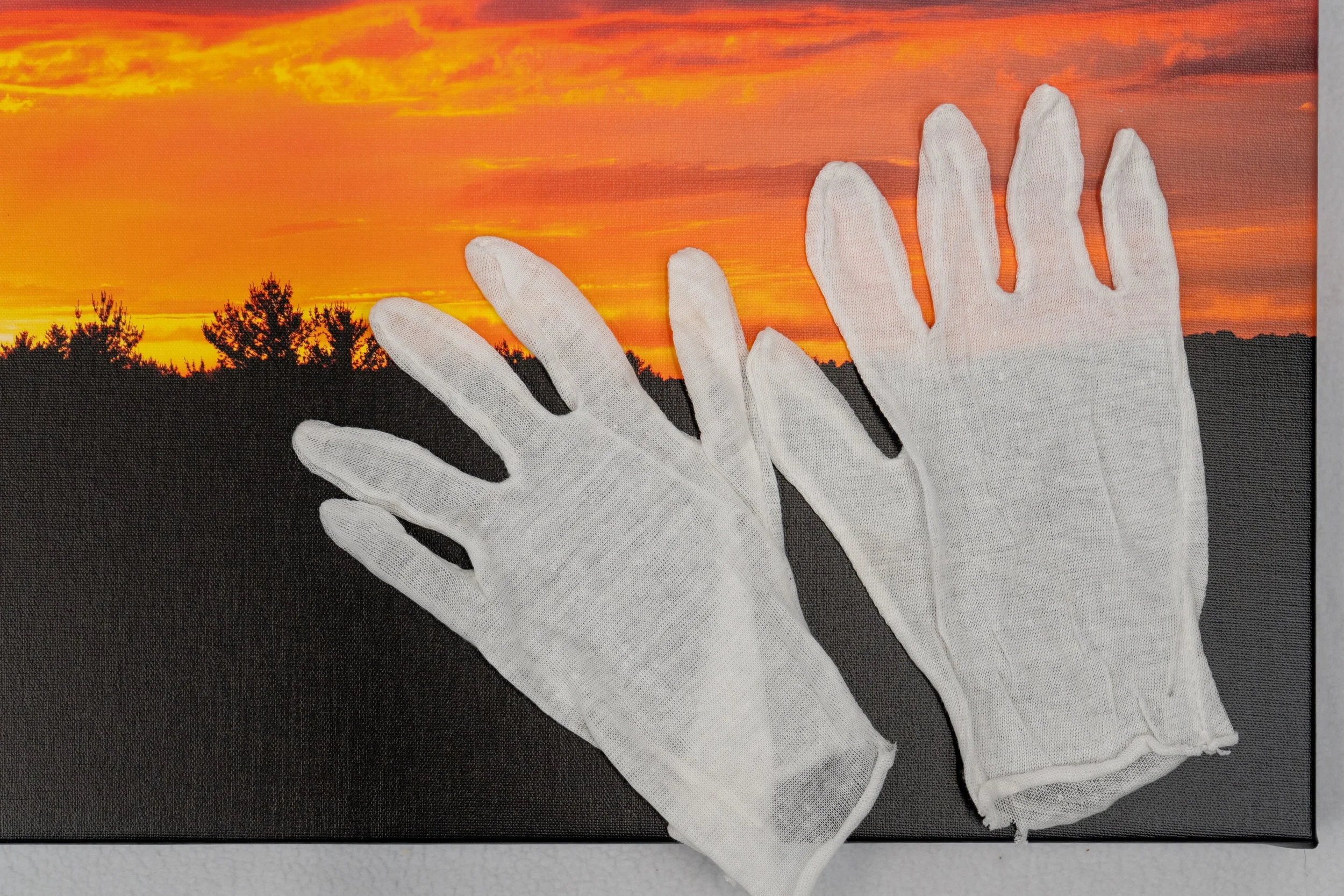 A pair of white gloves placed on a surface with a printed sunset scene featuring an orange sky and silhouette of trees.