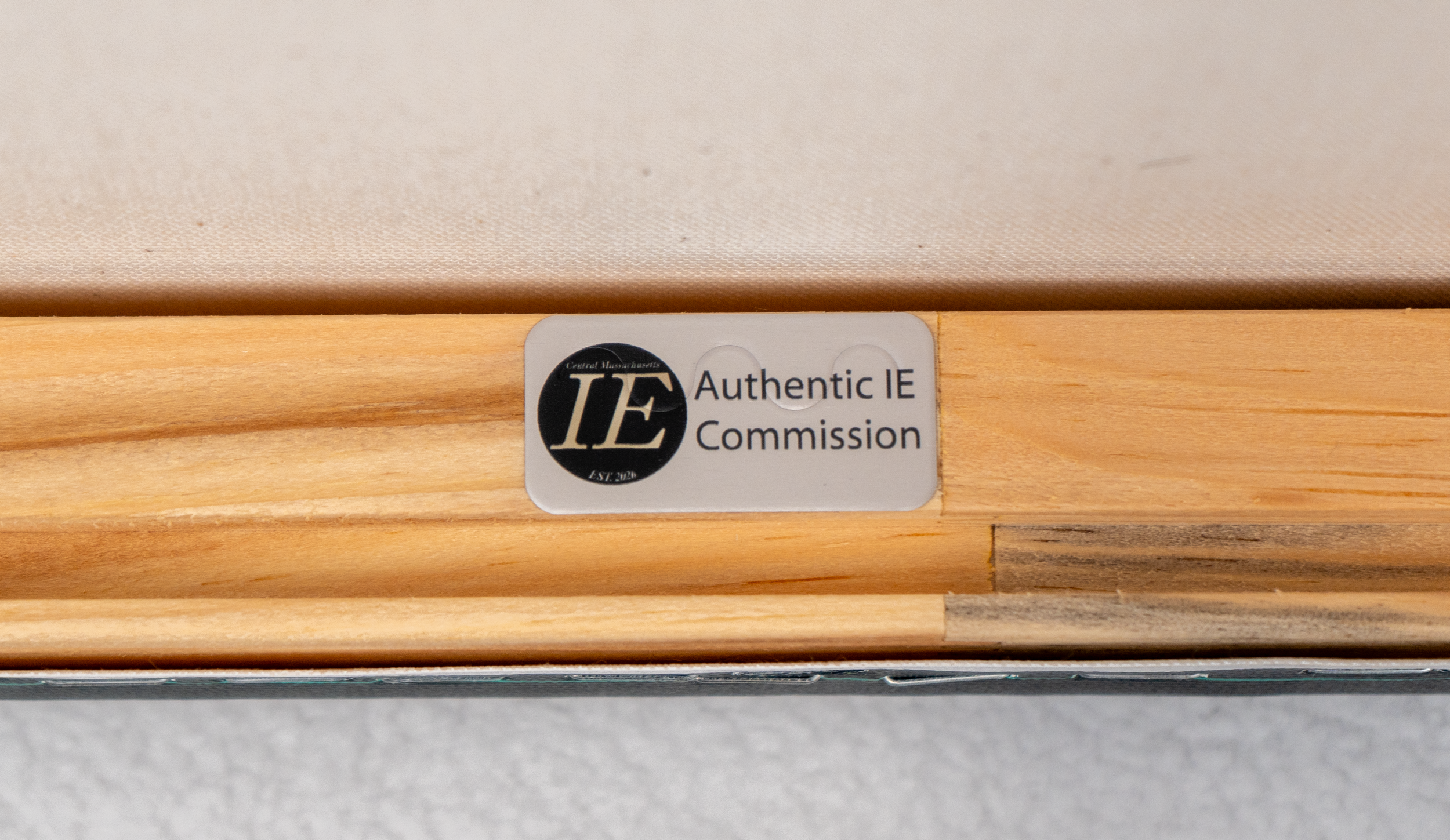 Close-up of a label on a wooden surface, reading 'Authentic IE Commission' with a logo featuring the letters 'IE' in a black circle.