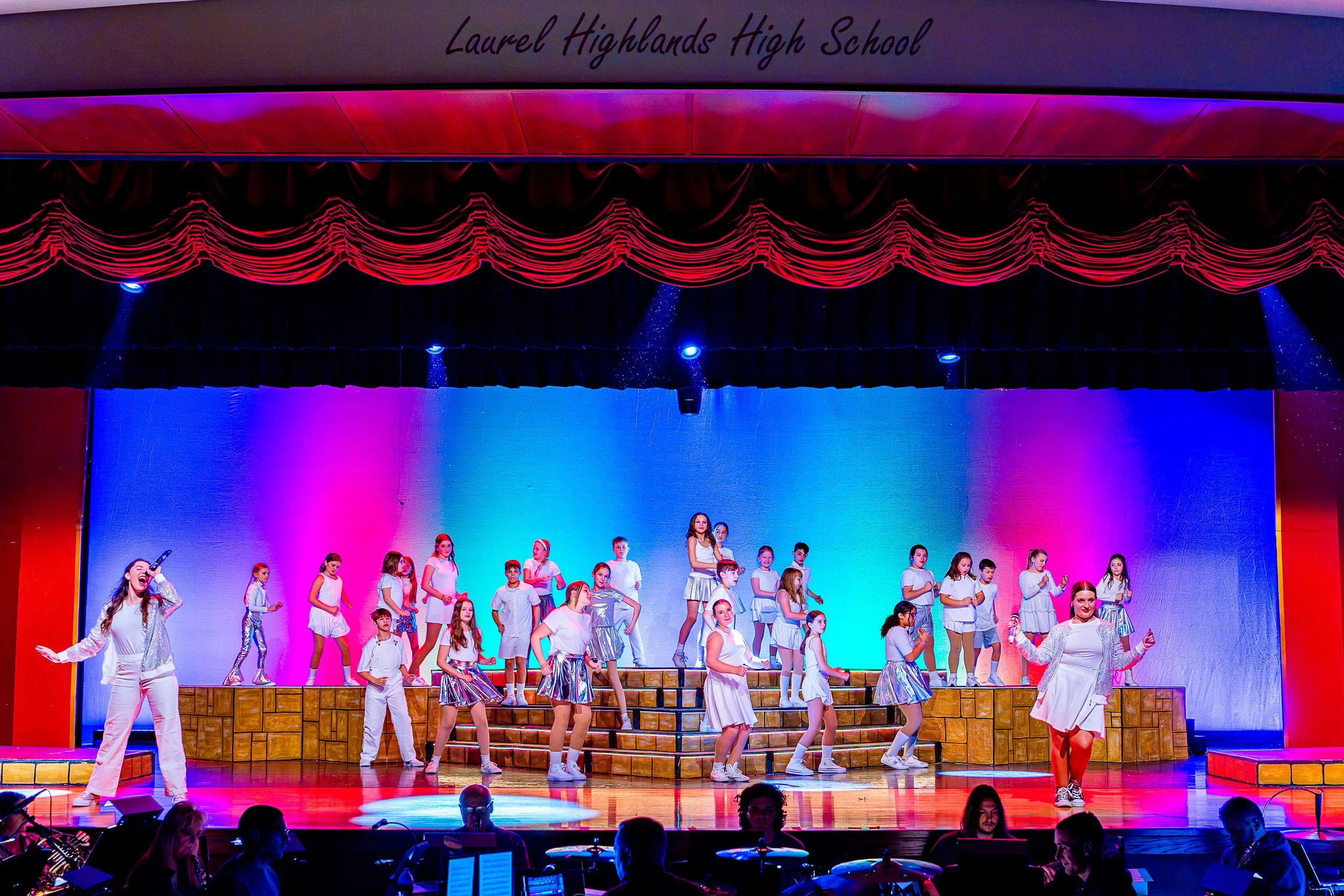 Singers and dancers on stage in front of a brightly colored set.