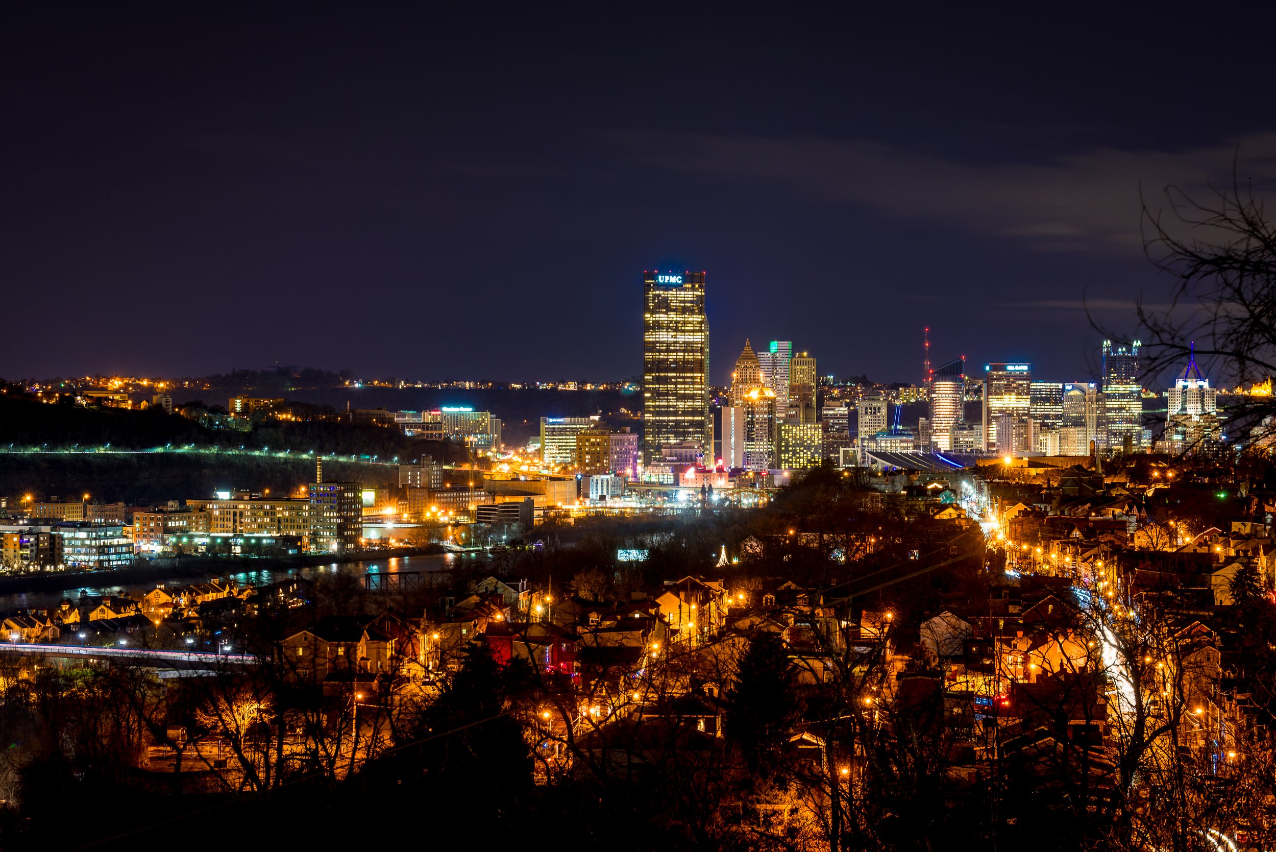 A night image of the Pittsburgh skyline with halogen streetlights in the foreground.