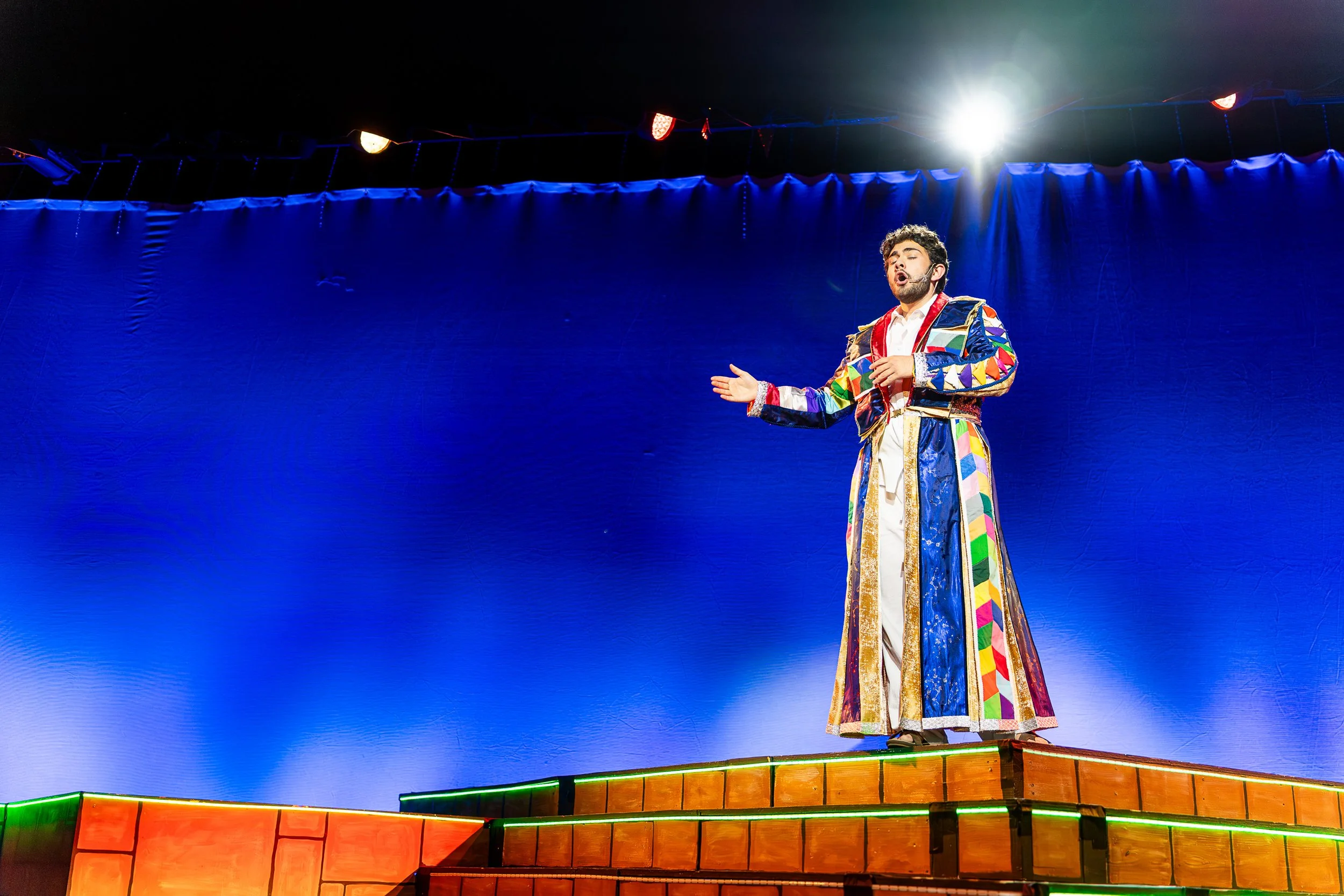 A person sings on stage while wearing a brightly colored coat.