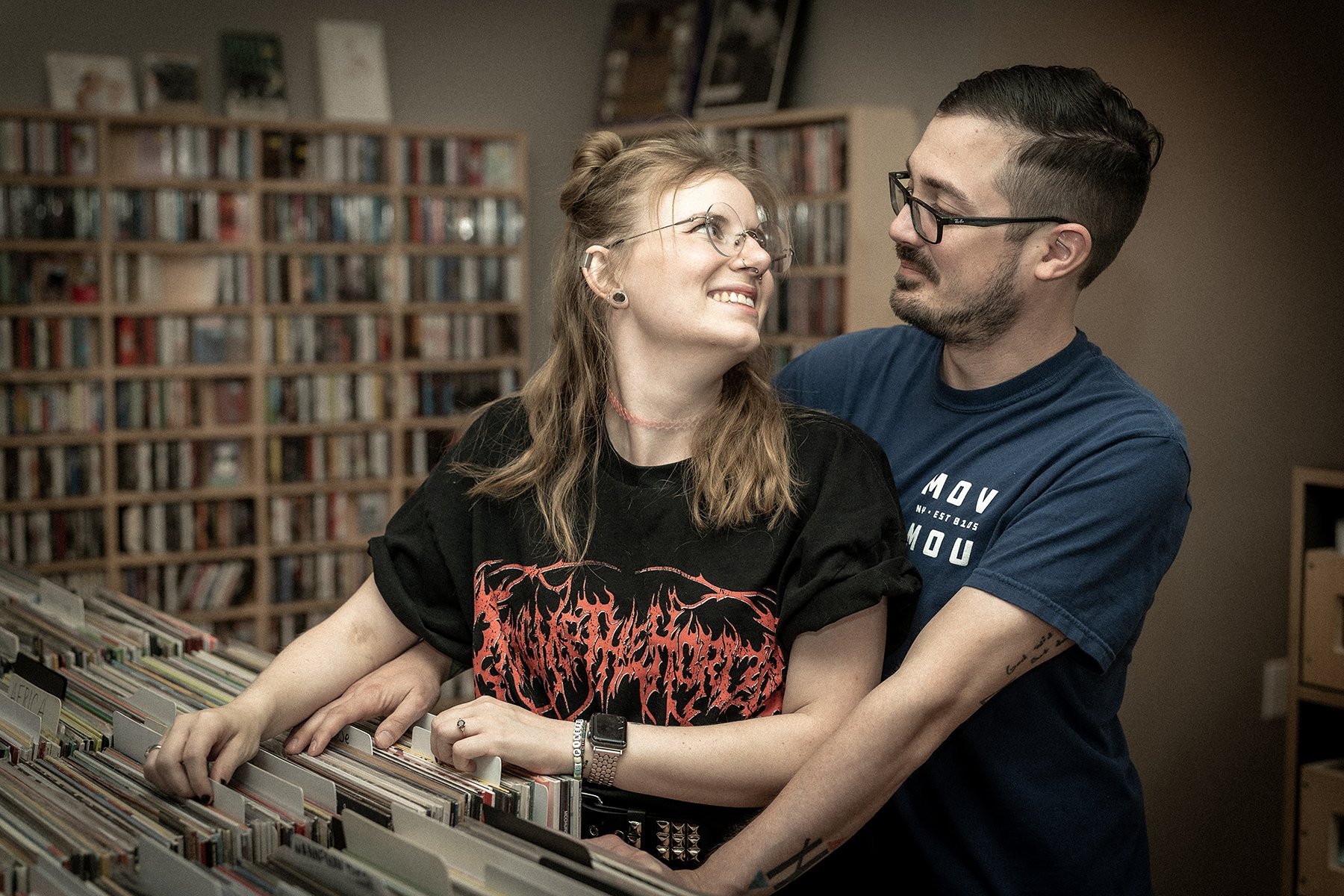 A couple stands together at a record bin, smiling at one another while searching through albums. Surrounded by shelves of records, the image captures a relaxed, affectionate moment and a shared love of music.