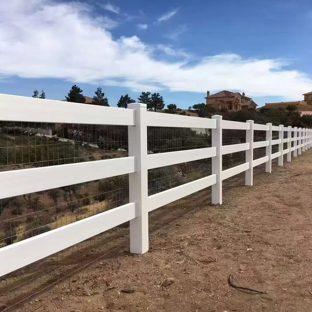White wooden fence with wire mesh in a rural area, with houses and trees in the background and a partly cloudy sky above.