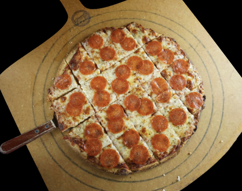 Pepperoni pizza cut into slices on a pizza board with a pizza cutter.