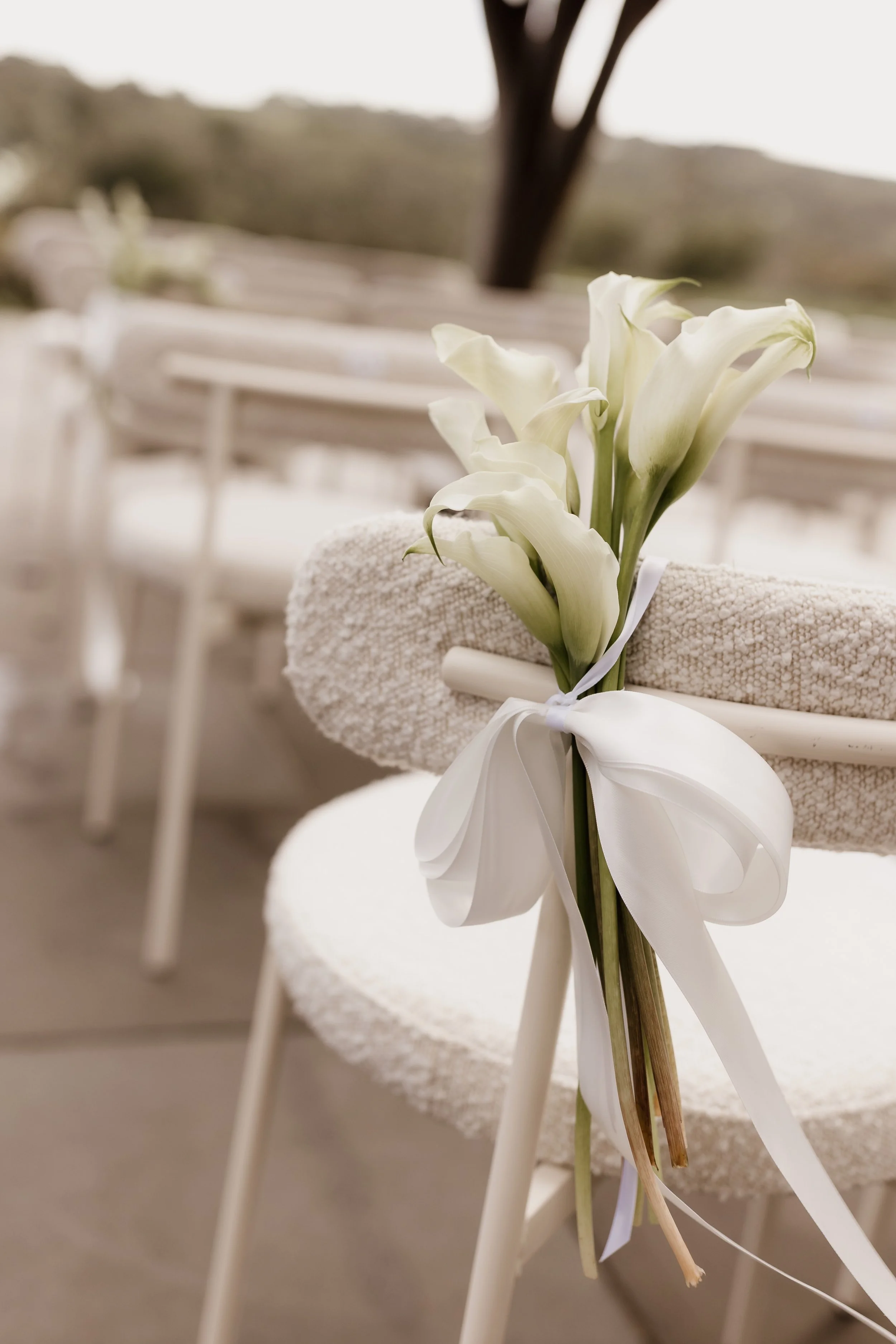 White calla lilies decorated on the back of a white chair, tied with a white ribbon, at Jackalope hotel wedding ceremony