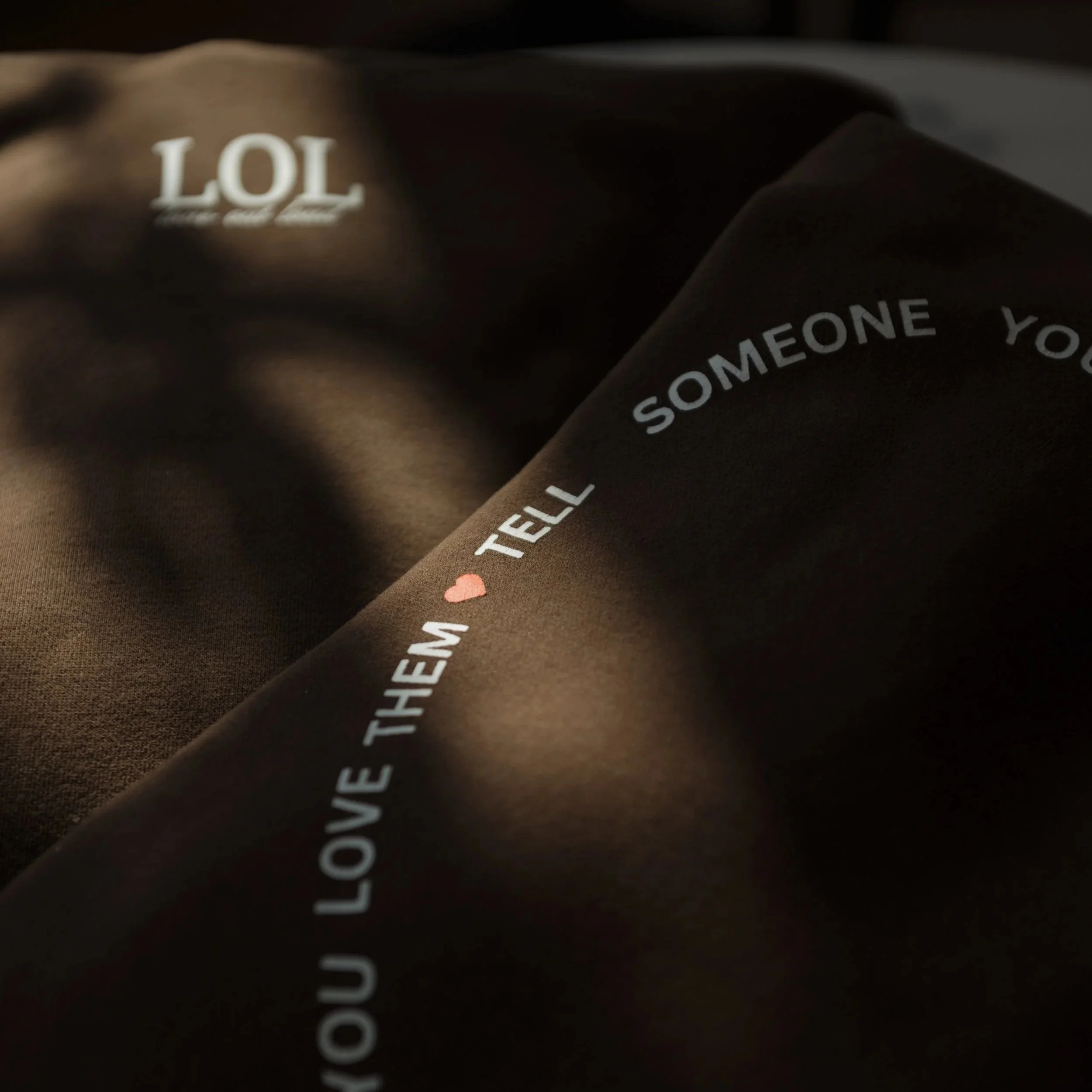 Close-up image of a dark surface with white text and a small pink heart. The visible text includes 'LOL' and part of a phrase, with some letters cut off.