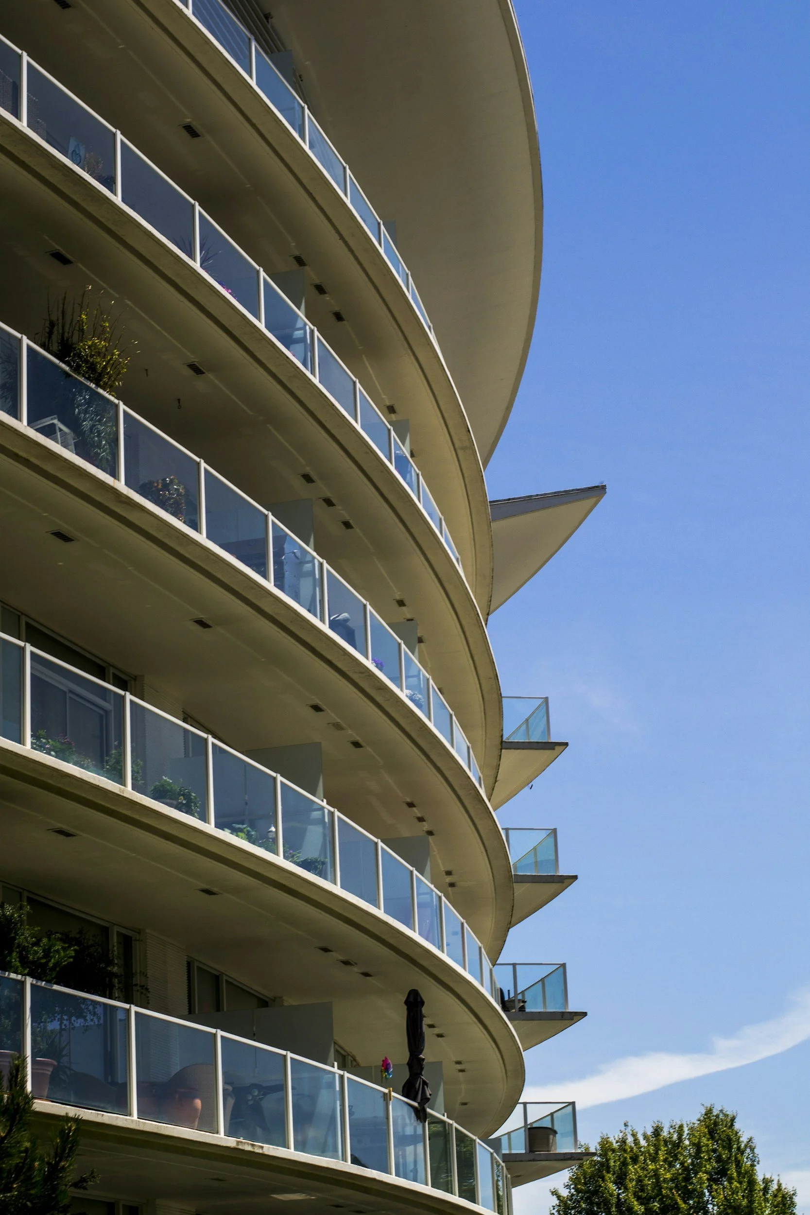 Close-up view of a modern multi-story apartment building with curved balconies and glass railings, set against a bright blue sky.