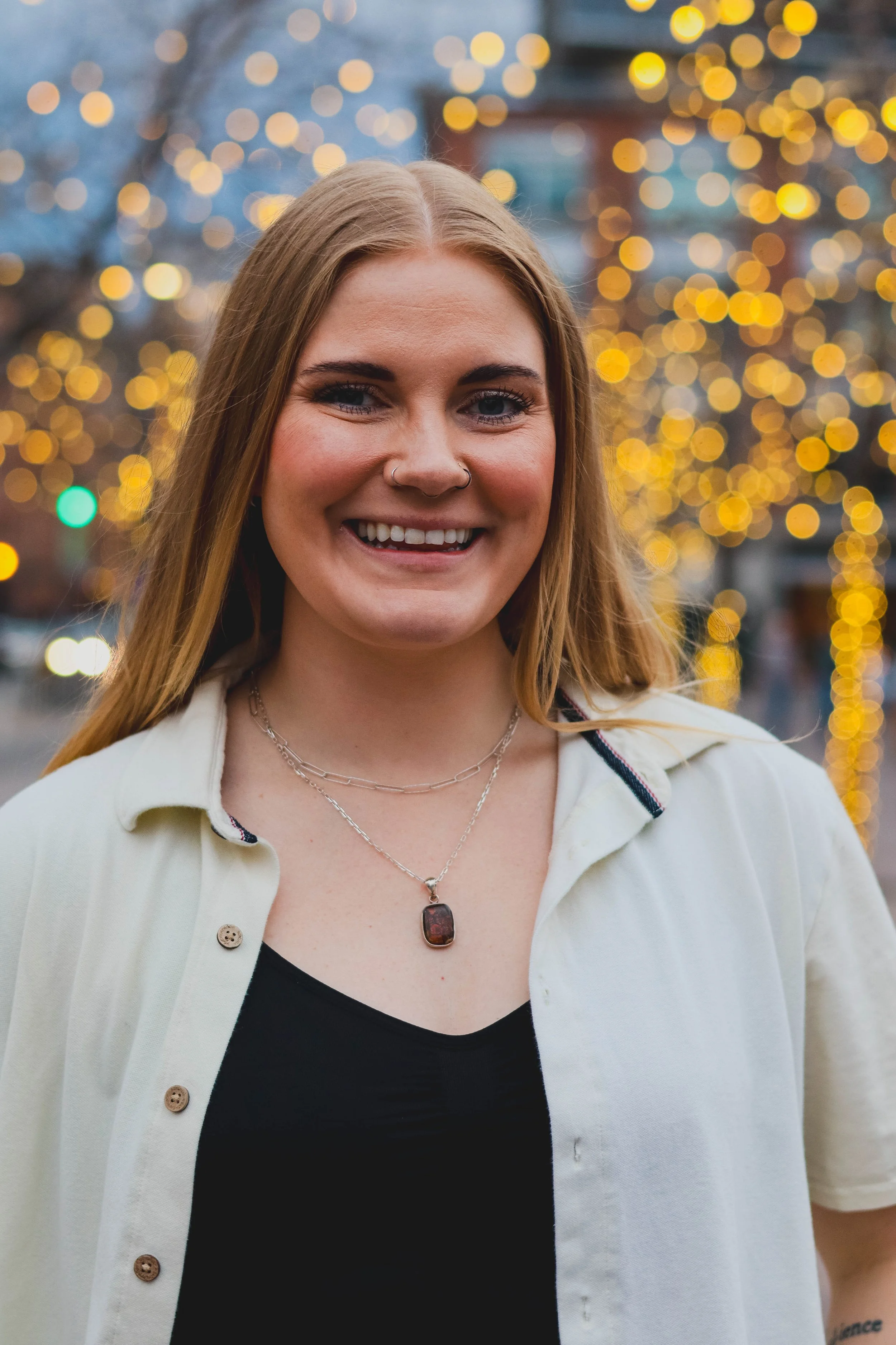 Sydney Cunfer, co-founder and Business Director of Rooted in More, smiling in front of a warm bokeh light background.