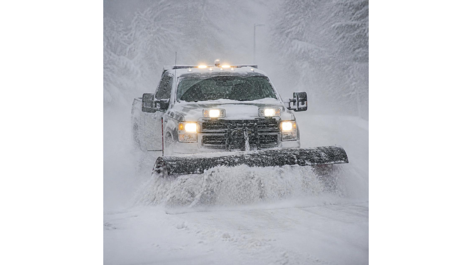 A snow plow clearing snow from a road during a snowstorm.