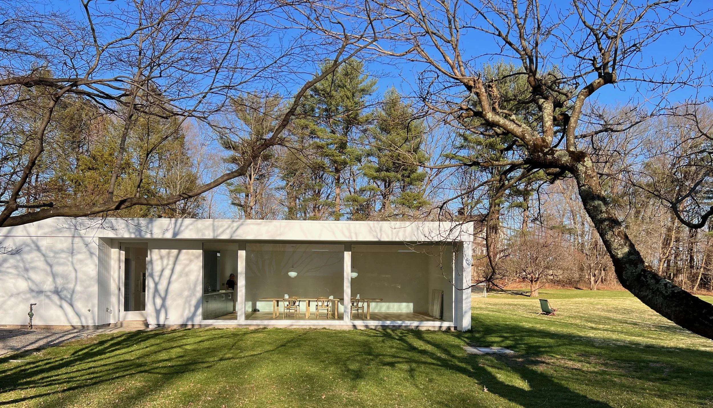 Modern white house with large glass windows, surrounded by trees and a green lawn, in a clear bright day.